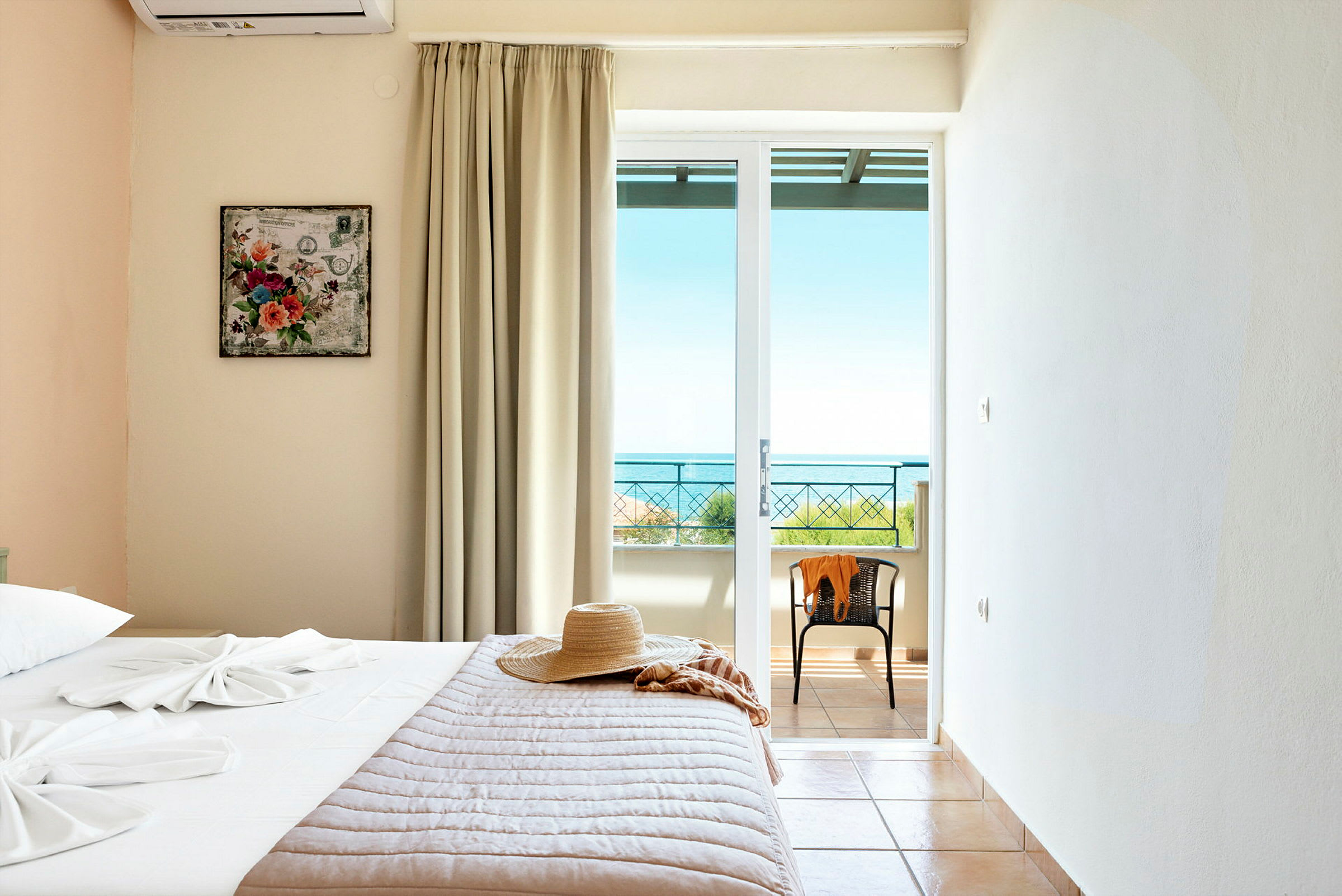 Ett hotellrum med en säng, en hatt och ett fönster med utsikt mot havet. (AI-genererad text)