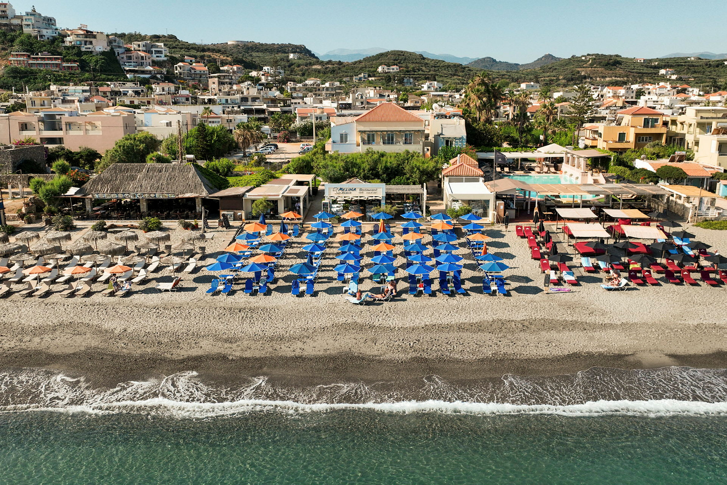 Strand med solstolar och parasoller, i bakgrunden byggnader. (AI-genererad text)