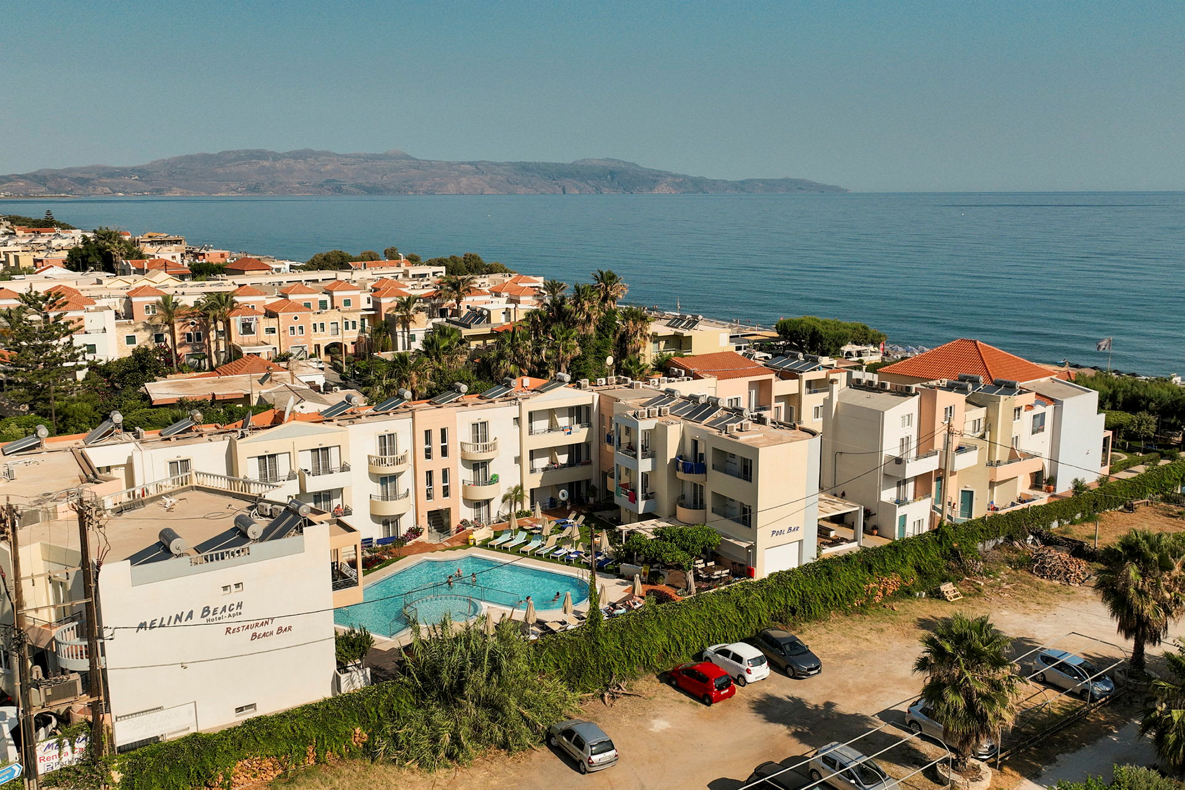 En vy över ett hotell med pool, beläget nära havet och omgivande byggnader. (AI-genererad text)