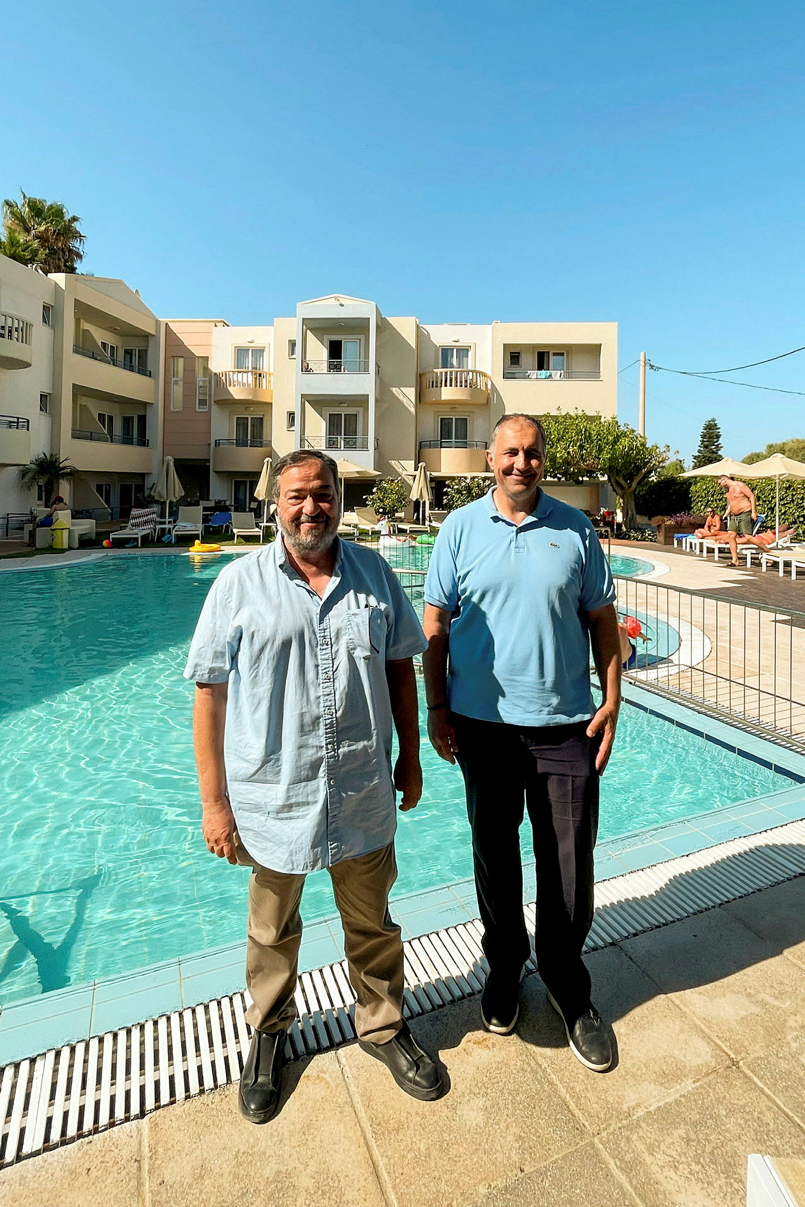 Personer står vid poolen framför ett hotell. (AI-genererad text)