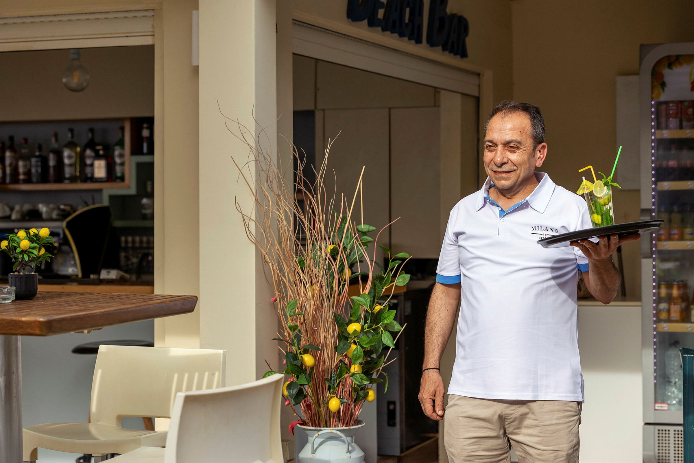 En servitör står vid en strandbar och håller en bricka med en drink. (AI-genererad text)