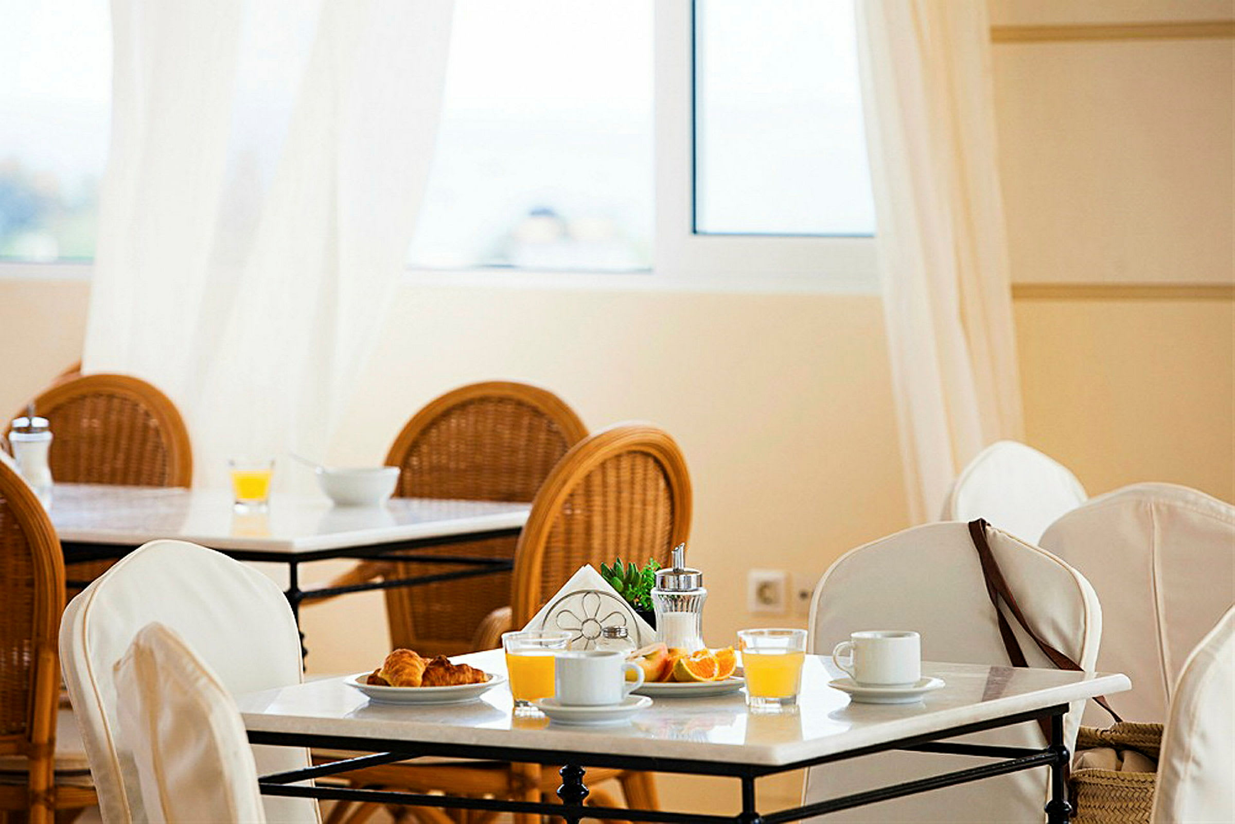 En frukostplats med uppdukade bord, vita dukar och frukostartiklar som juice, kaffe och bröd. (AI-genererad text)