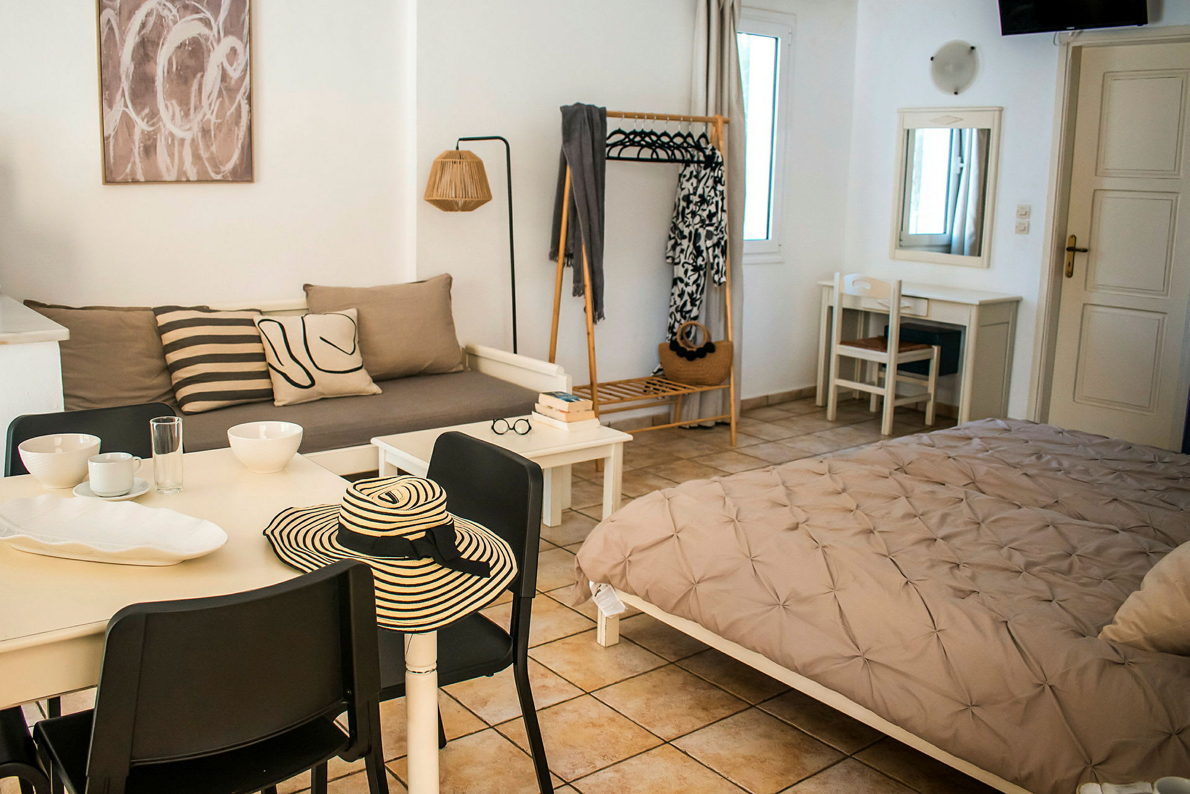 Ett stilrent möblerat rum med en liten matplats, soffa, säng och klädhängare. (AI-genererad text)