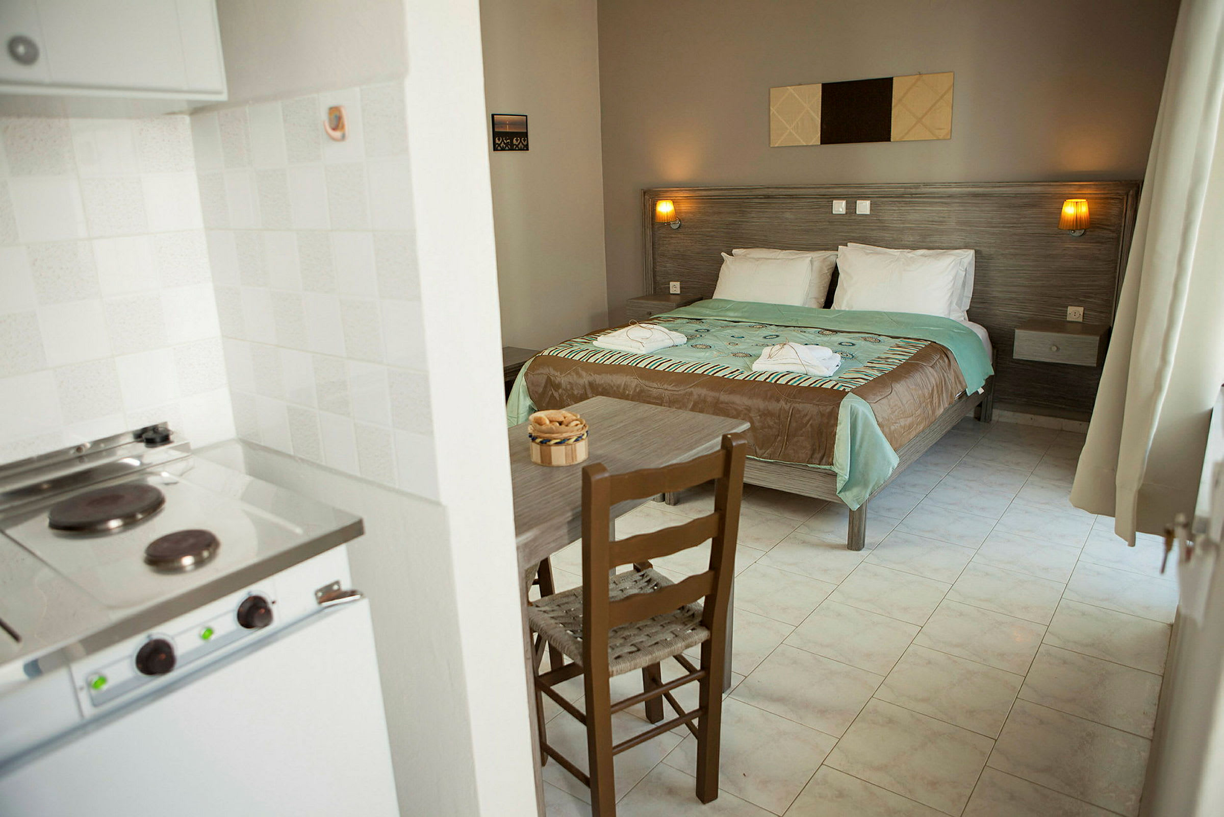Ett hotellrum med dubbelsäng, bord, stol och en liten köksyta. (AI-genererad text)