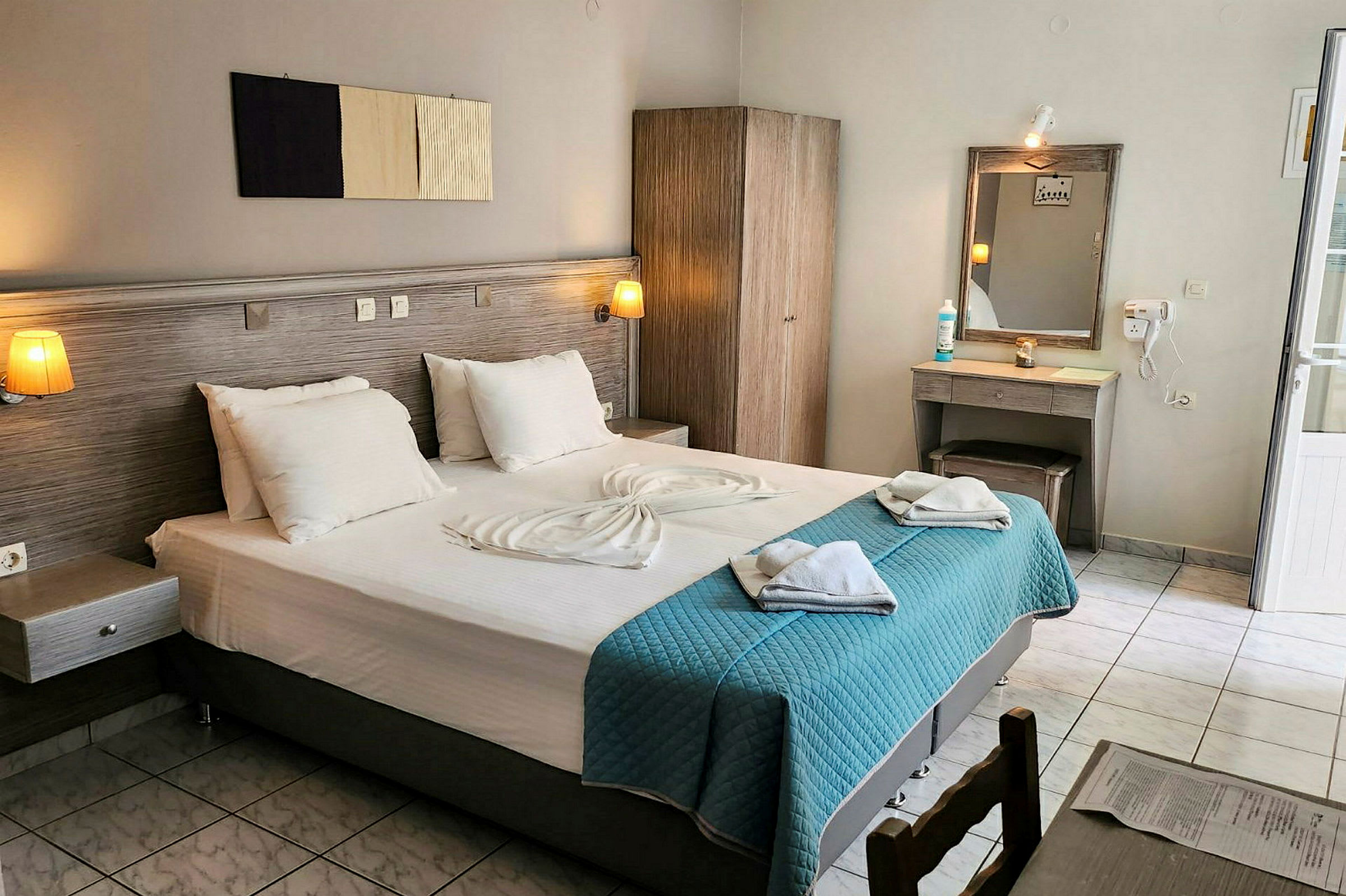 Hotellrum med en dubbelsäng, garderob, sminkbord, och ljusa textilier. (AI-genererad text)