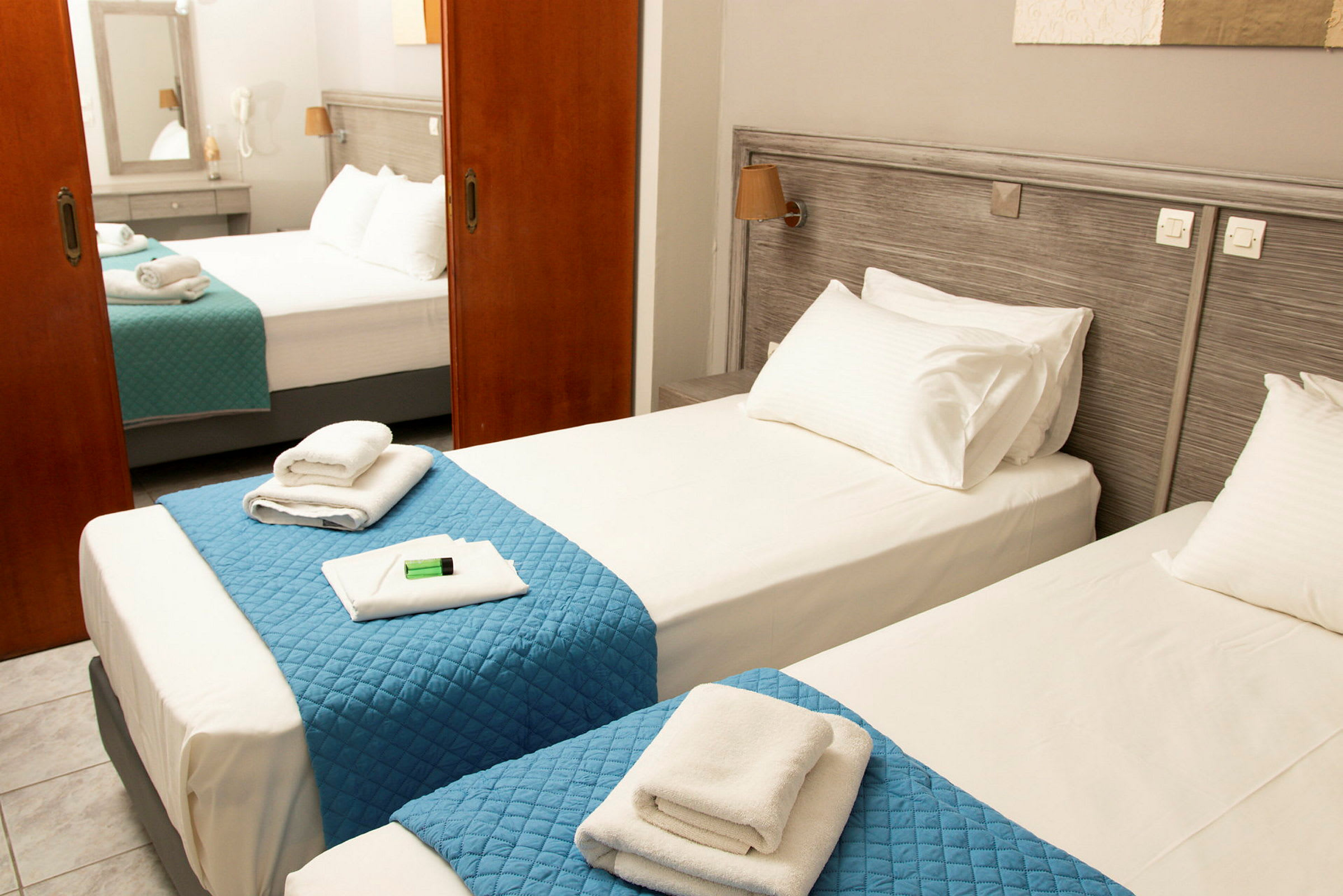 Ett hotellrum med två enkelsängar utrustade med blåa täcken och vita handdukar. (AI-genererad text)