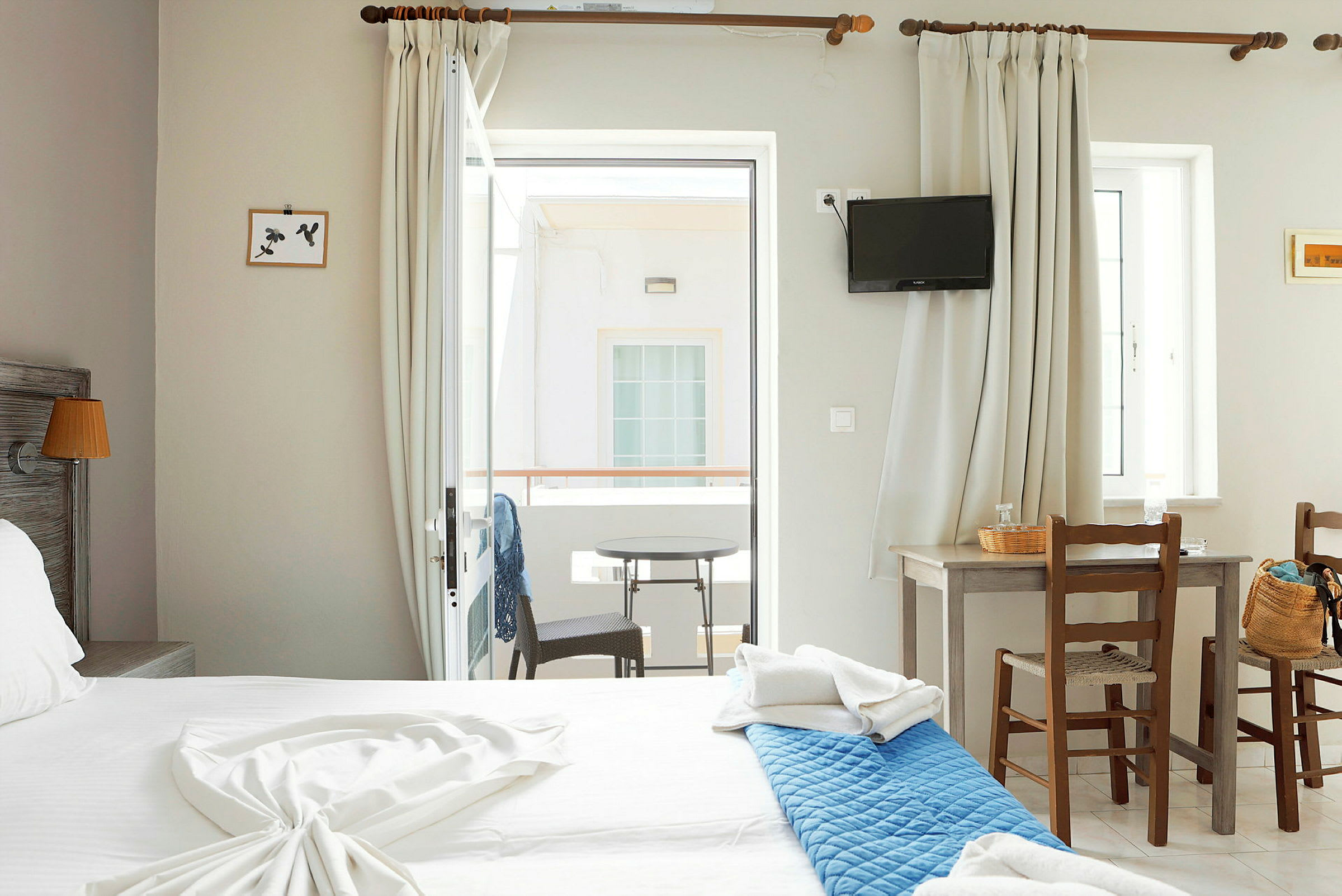 Interiör av ett hotellrum med en dubbelsäng, ett bord med två stolar och en balkong med utsikt. (AI-genererad text)