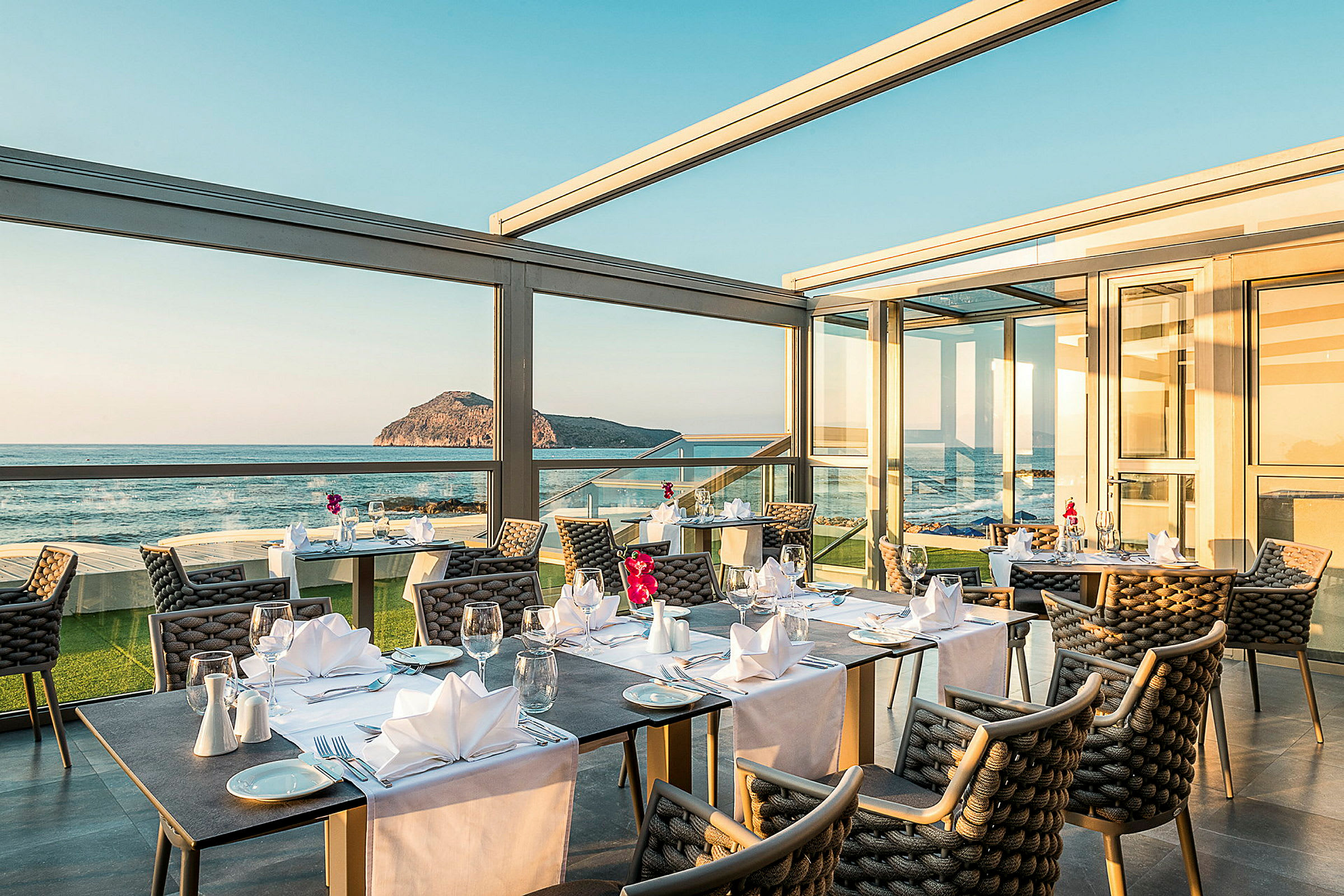 Restaurang med bord som är dukade och stor fönsterutsikt mot hav och landskap. (AI-genererad text)