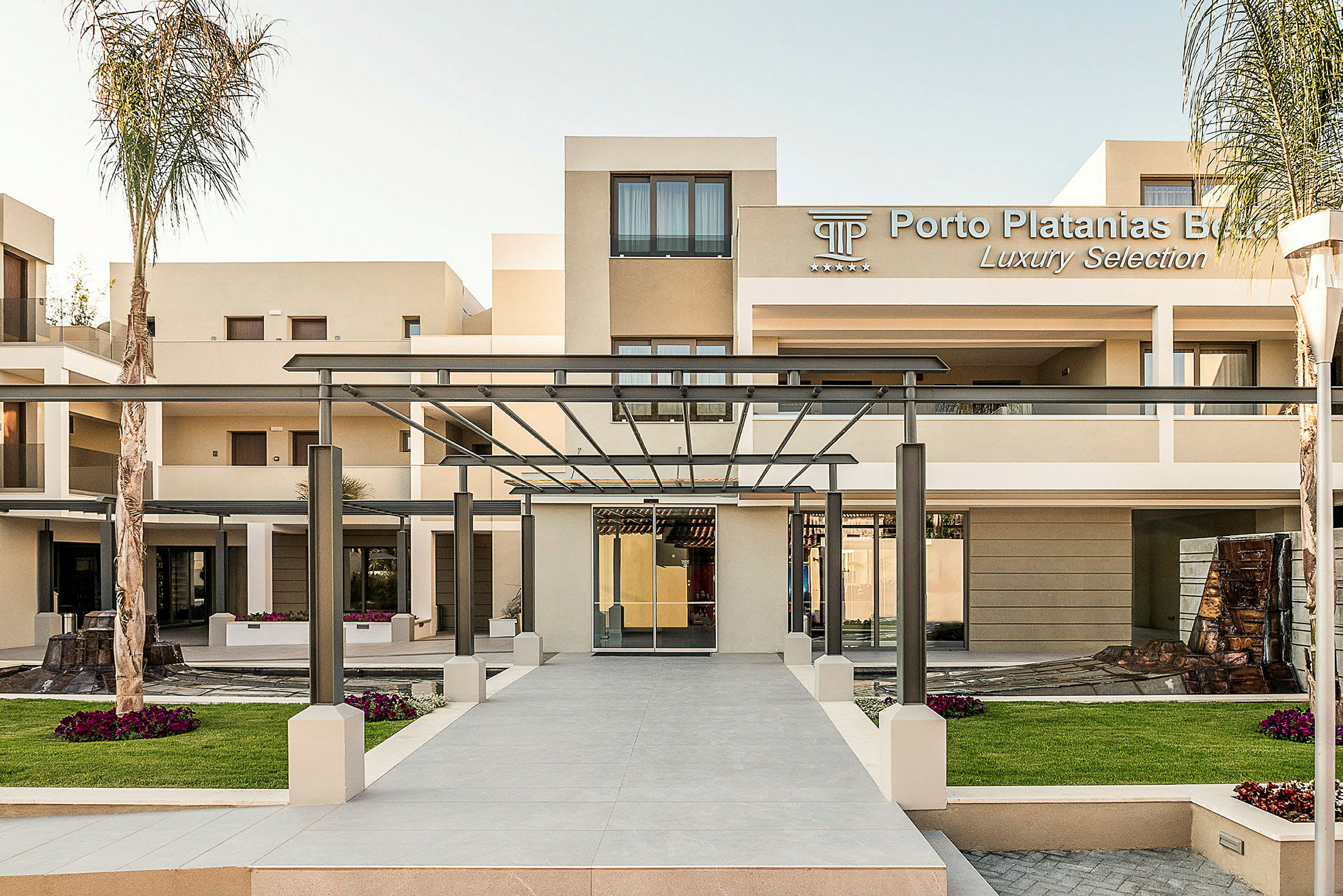 Entré till Porto Platanias Beach Resort med moderna byggnader och en pergola. (AI-genererad text)