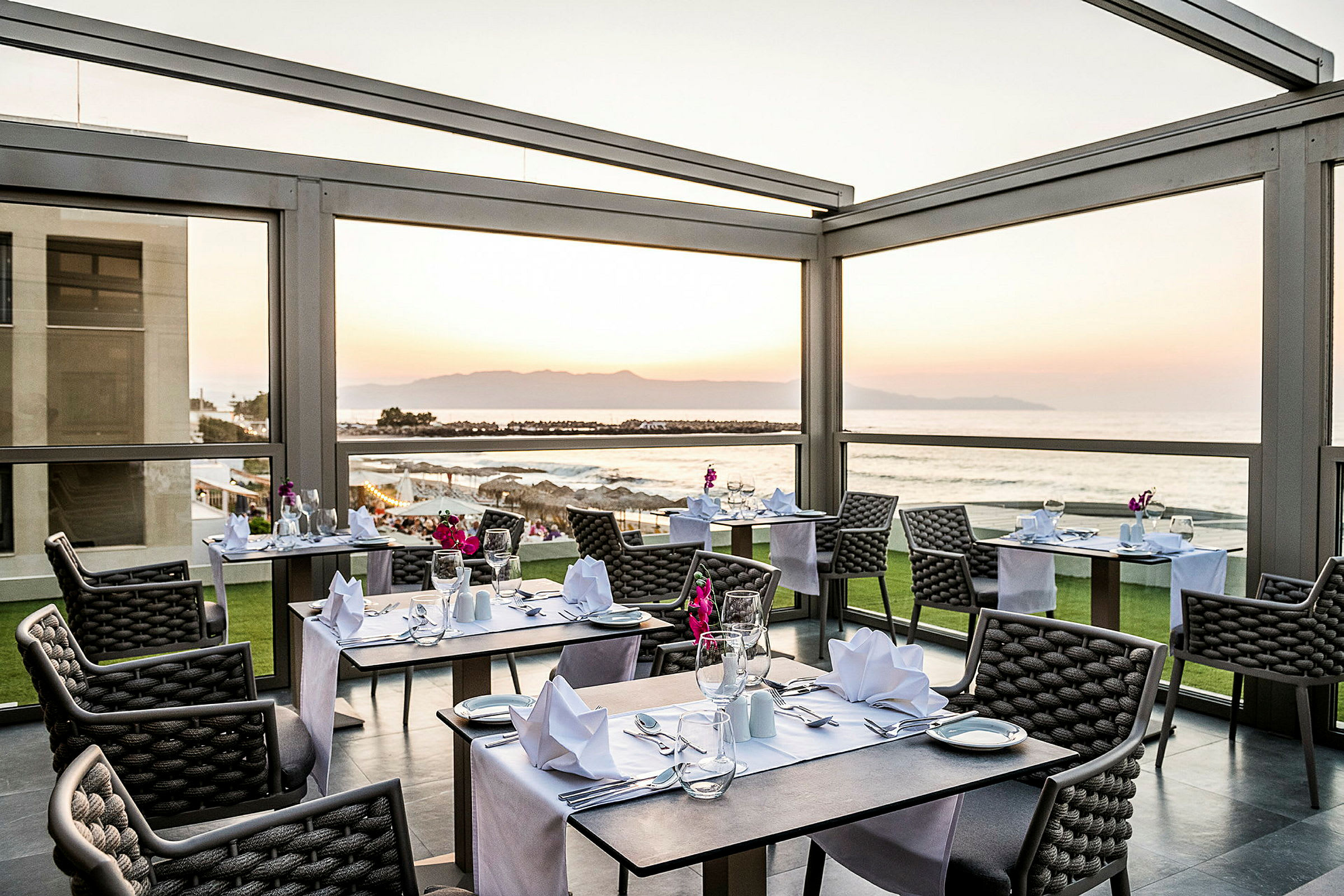 Ett restaurangområde med uppdukade bord och utsikt över havet vid solnedgången. (AI-genererad text)