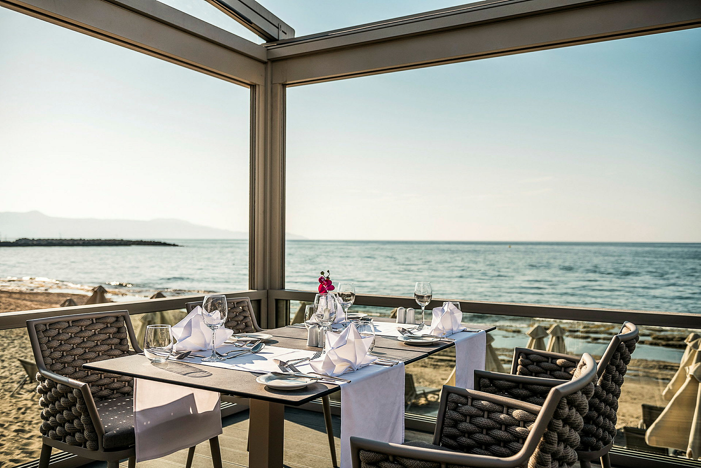 En restaurangplats vid havet med dukade bord och utsikt över stranden. (AI-genererad text)
