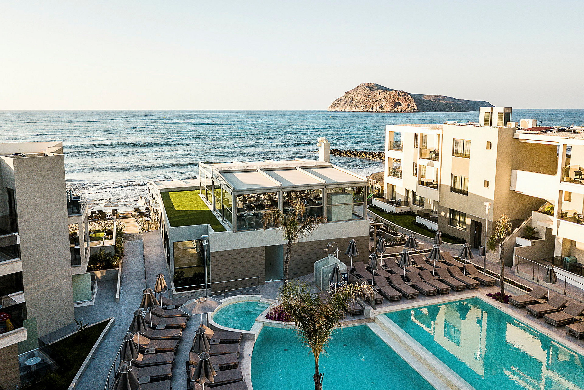 Hotellbyggnader med pool och solstolar nära havet. (AI-genererad text)