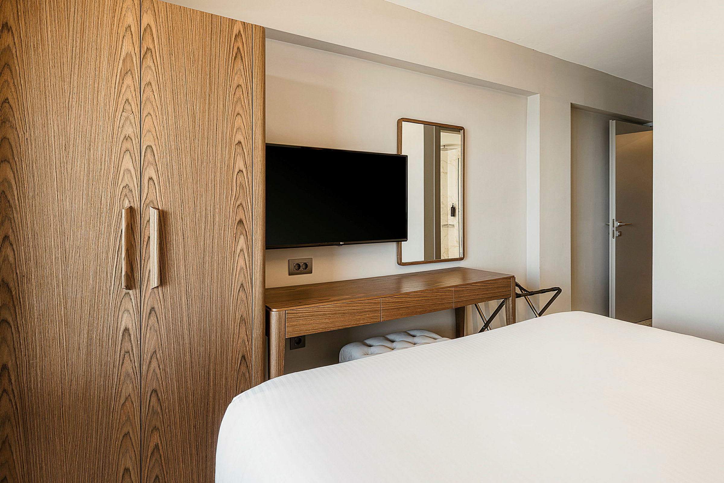 Ett hotellrum med en garderob i trä, en TV på väggen och ett skrivbord med spegel. (AI-genererad text)