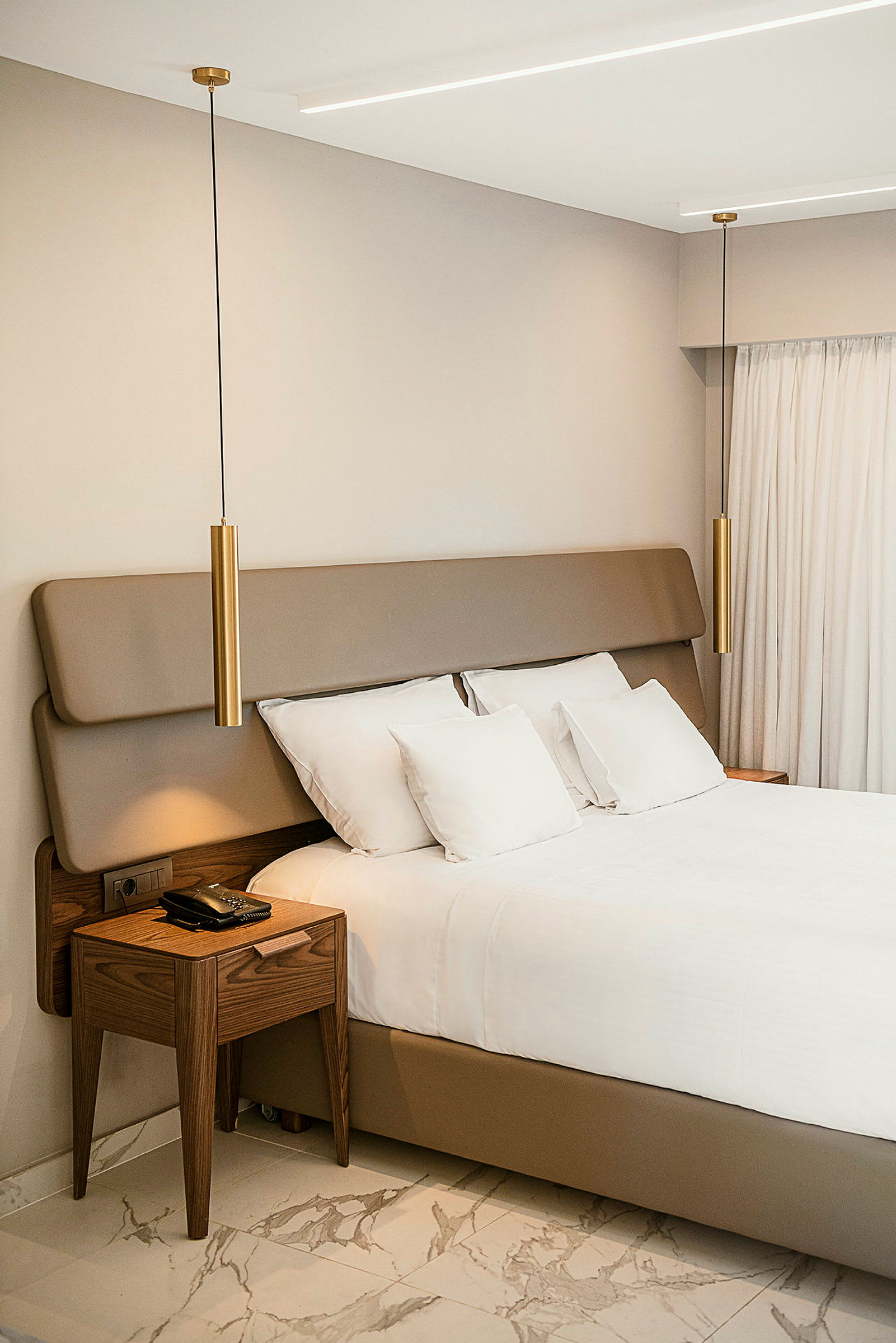 Ett modernt och stilrent hotellrum med en säng, träbord och hängande lampor. (AI-genererad text)
