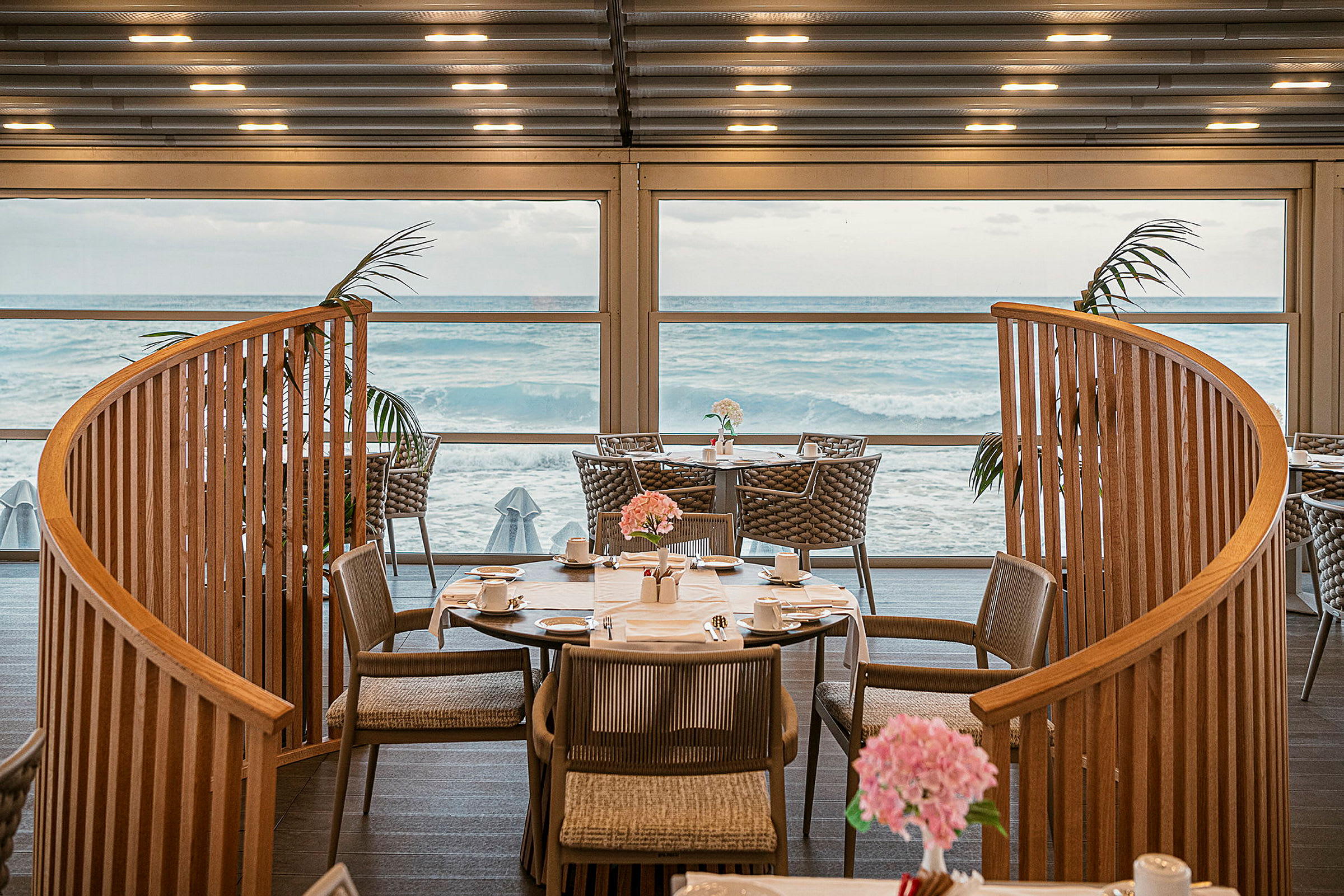 Interiör av en restaurang med utsikt över havet genom stora fönster. (AI-genererad text)