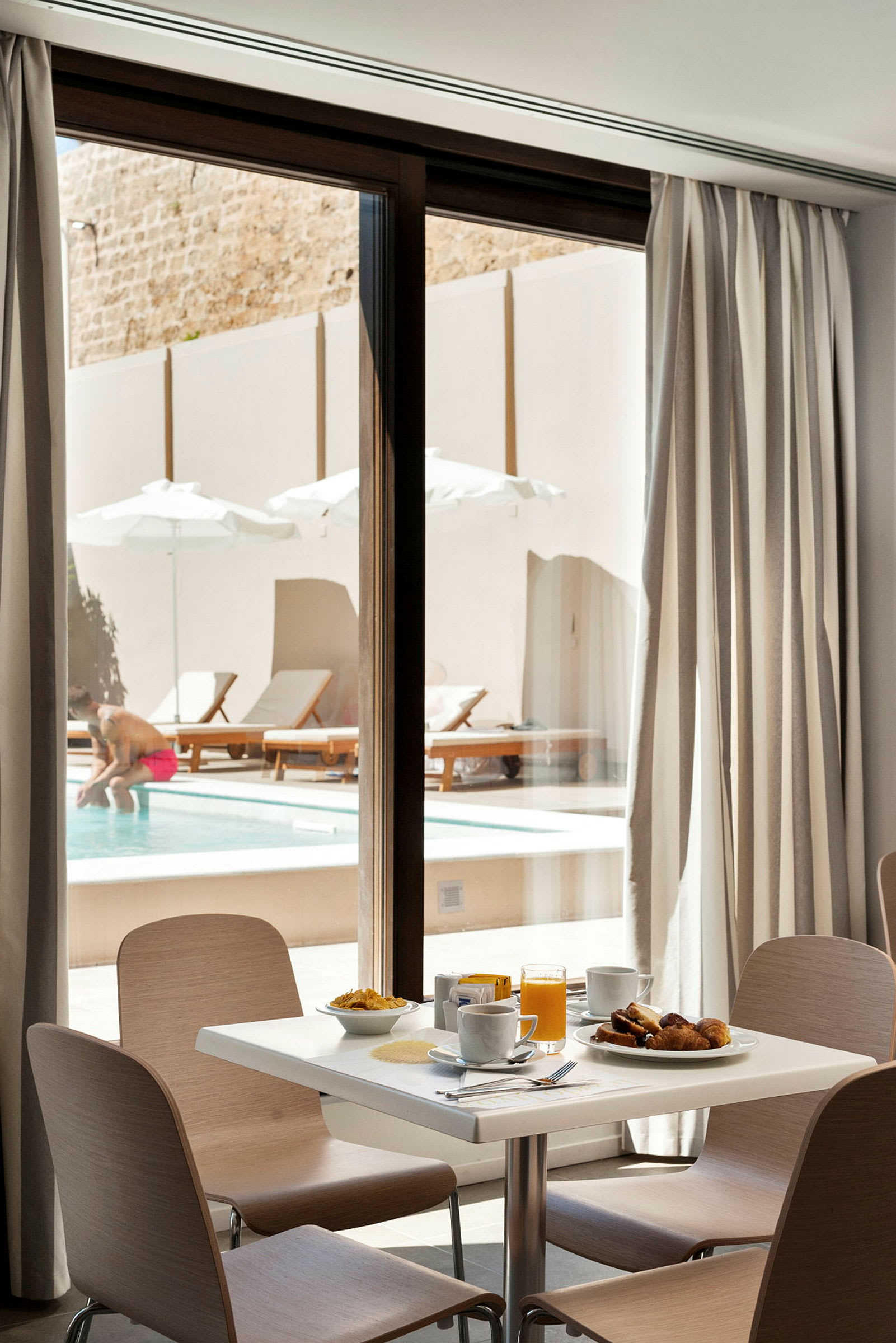 Frukostbord med utsikt mot en pool och solstolar utanför. (AI-genererad text)