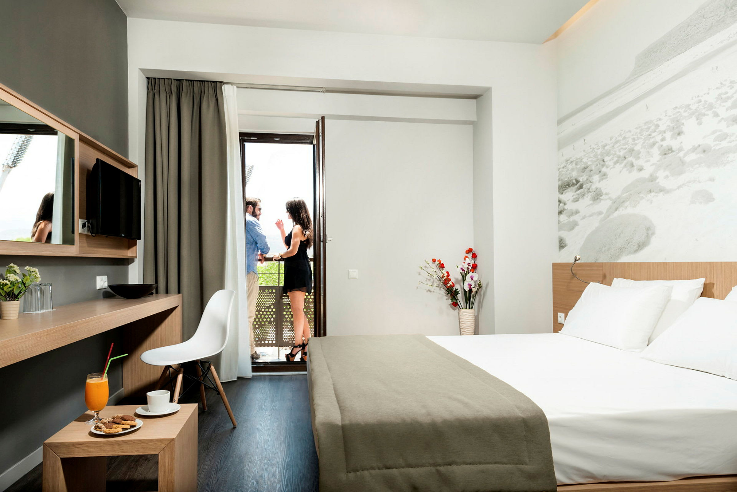 Modernt hotellrum med en dubbelsäng, skrivbord och utsikt mot en balkong. (AI-genererad text)