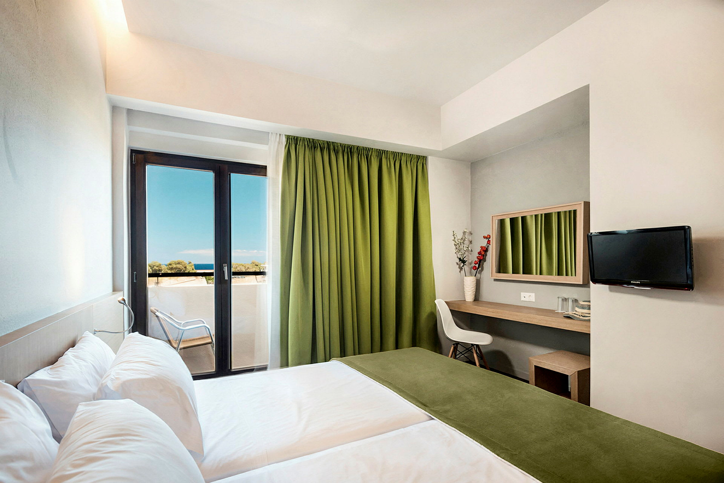 Ett hotellrum med två sängar, en arbetsyta med spegel, en stol och en TV på väggen. Rummet har en balkong med gröna gardiner och utsikt mot havet. (AI-genererad text)