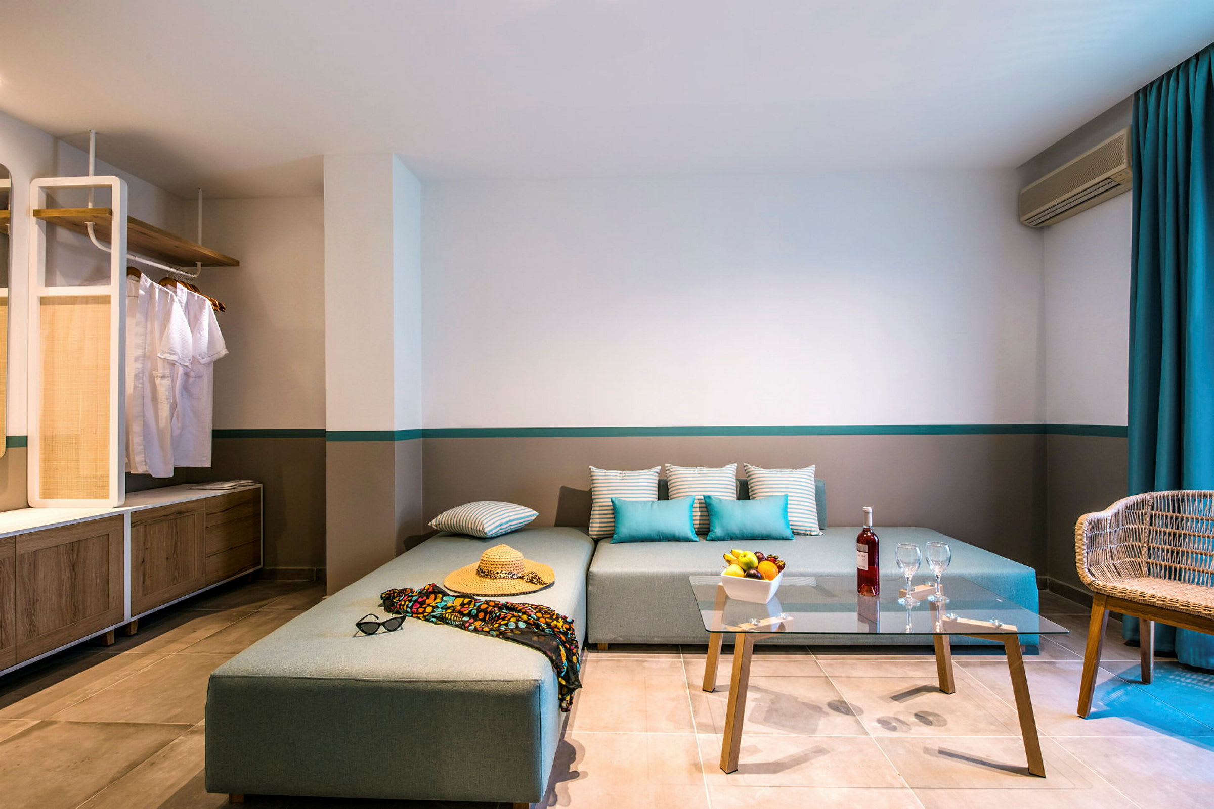 Modernt hotellrum med hörnsoffa, glasklart soffbord och avslappnad inredning. (AI-genererad text)
