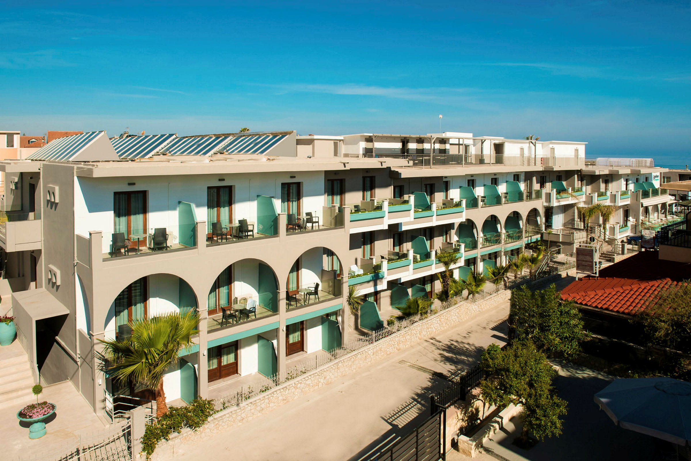 Bild av ett hotell med balkonger och arkitektoriska valv, omgiven av grönska. (AI-genererad text)