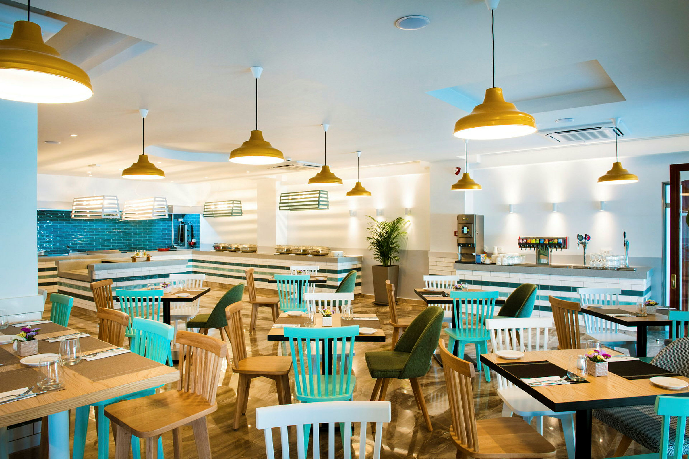 Ett ljust inrett restaurangområde med bord och stolar, samt gula taklampor. (AI-genererad text)