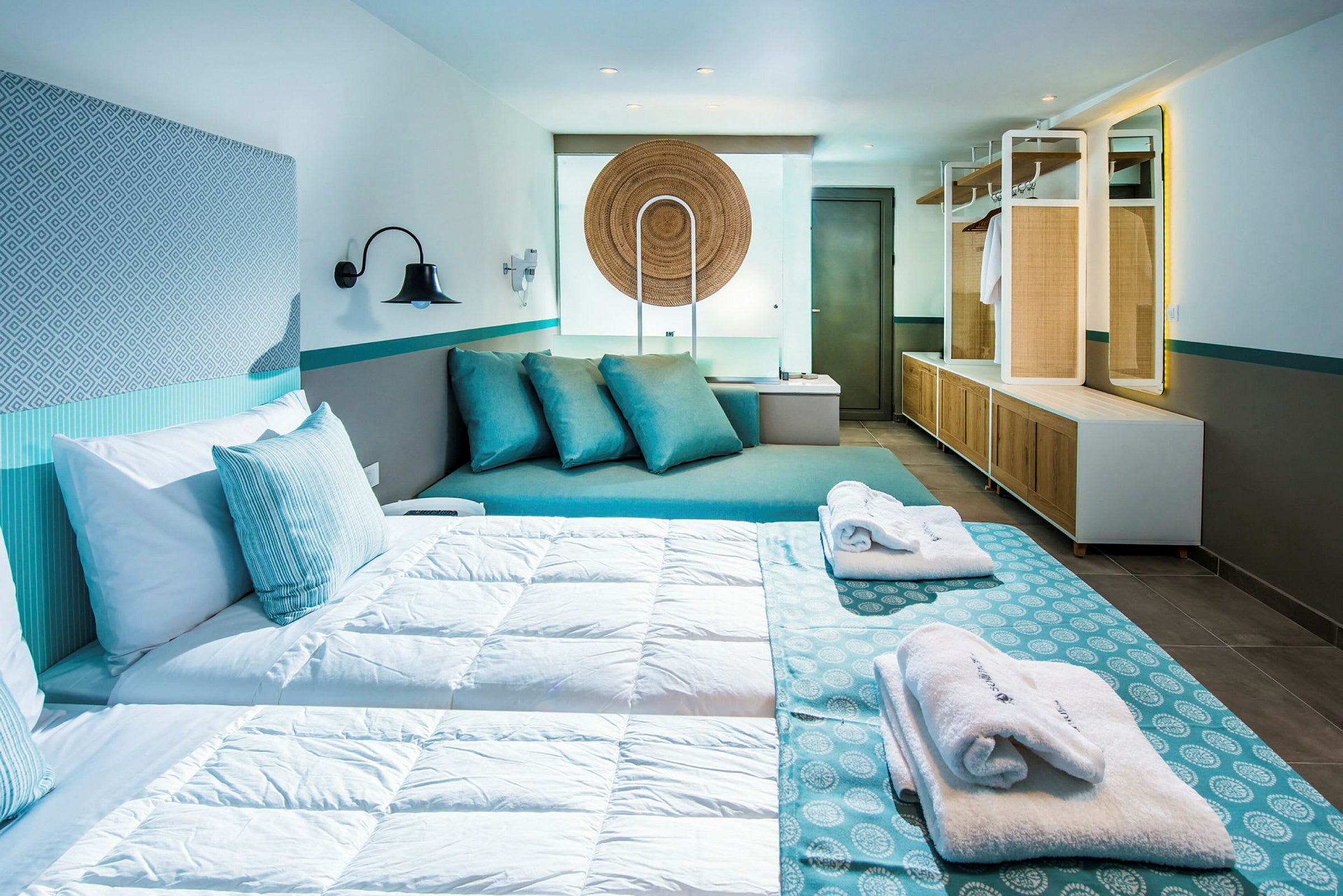 Ett modernt hotellrum med en dubbelsäng, dekorerat i blå och vita färger, sittutrymme med kuddar och garderob. (AI-genererad text)