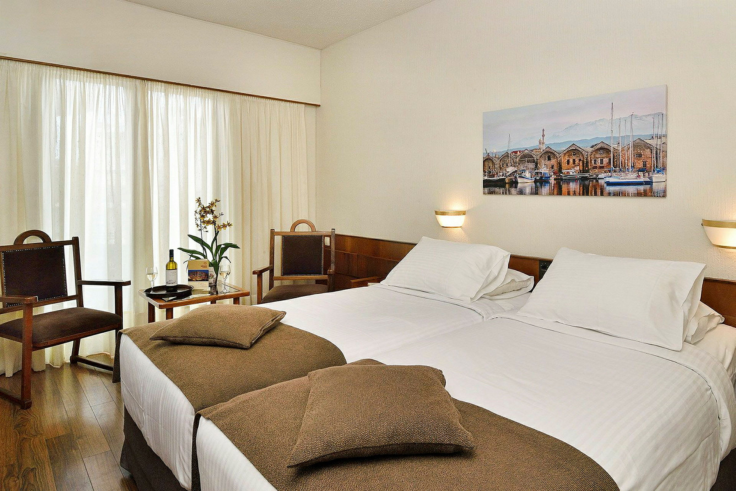 Hotellrum med dubbelsäng, två stolar och en tavla av ett hamnmotiv. (AI-genererad text)