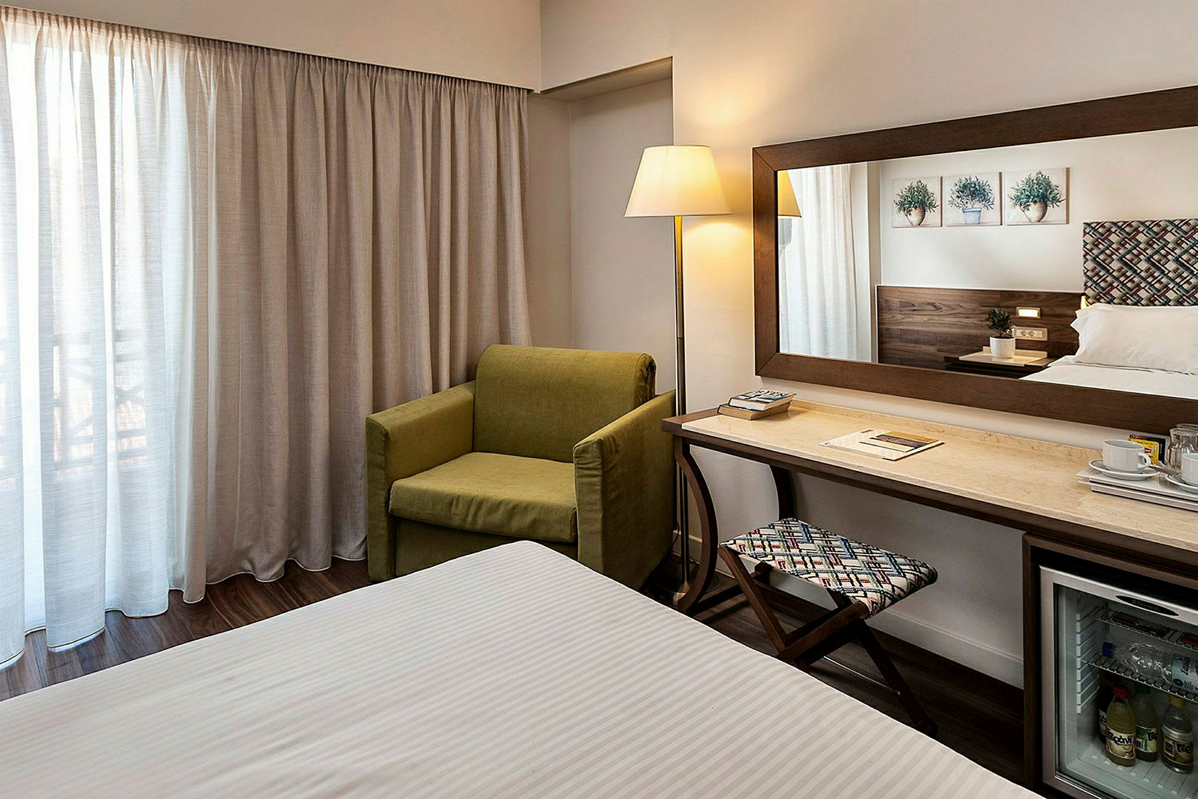 Hotellrum med grön fåtölj, skrivbord, spegel och säng. (AI-genererad text)