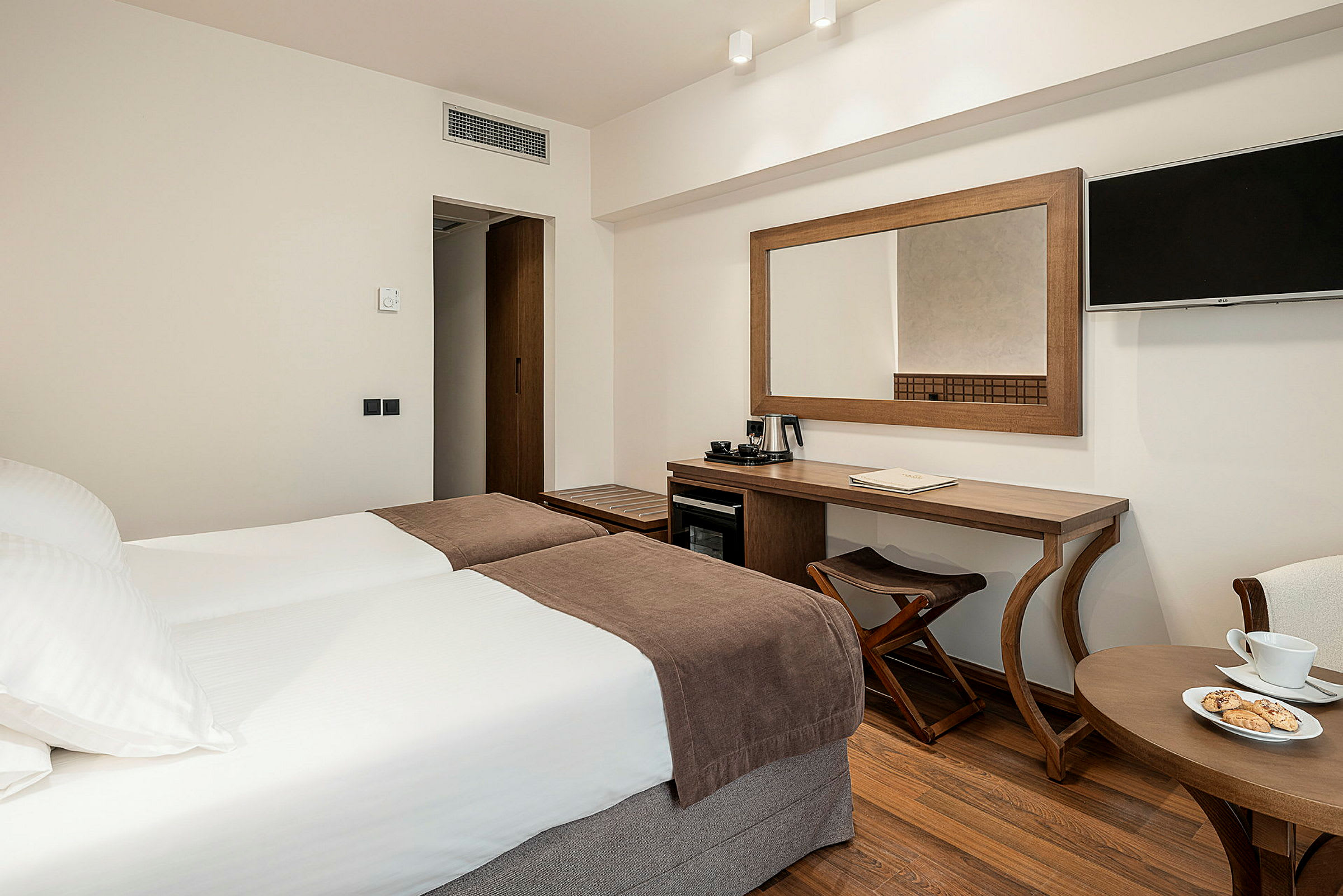 Hotellrum med två enkelsängar, skrivbord, väggmonterad TV och en kaffekokare. (AI-genererad text)