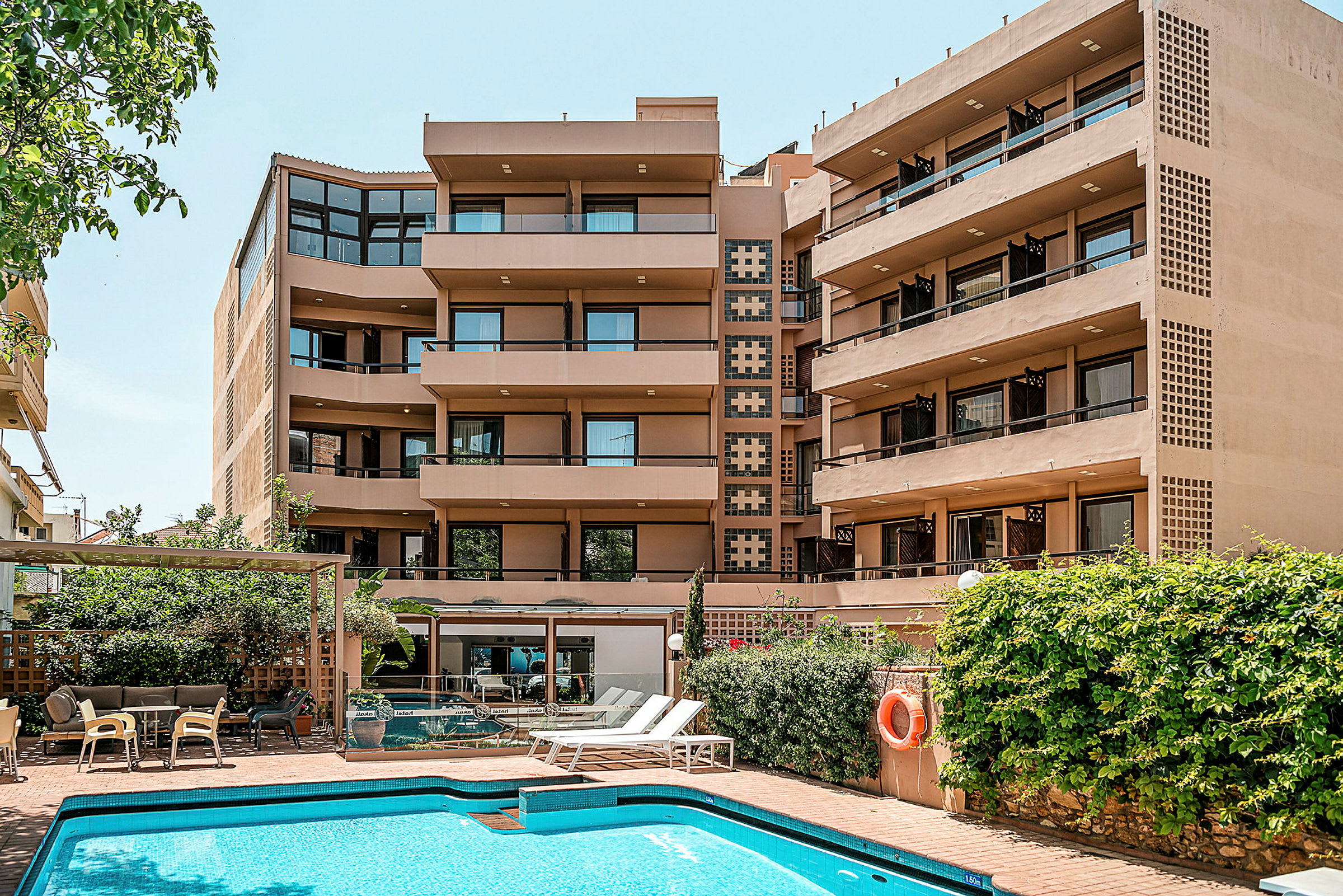 Bild av ett hotell med flera våningar och en pool omgiven av solsängar och grönska. (AI-genererad text)