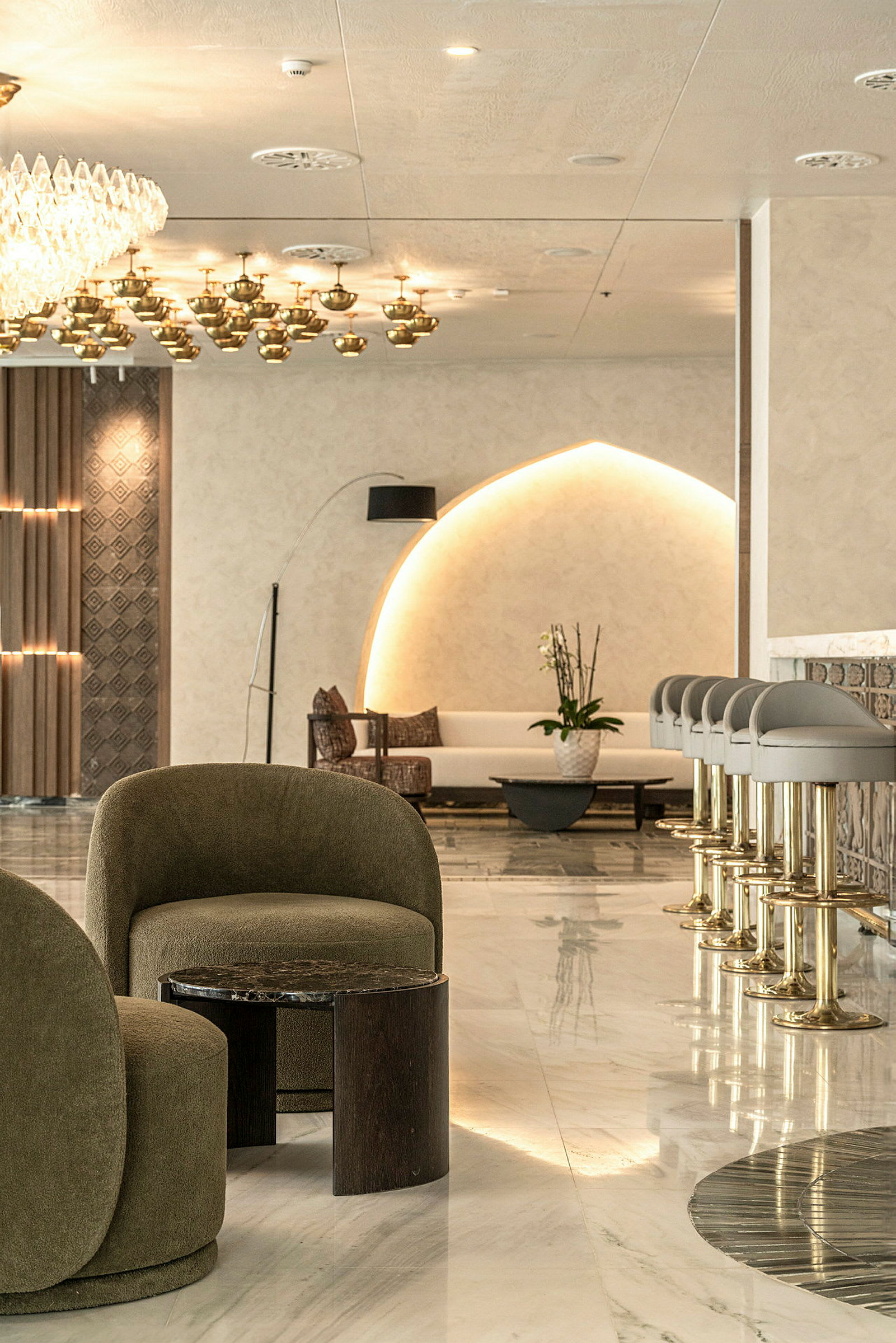 Ett elegant hotelllobby med moderna möbler, inklusive gröna fåtöljer och en rad barstolar. (AI-genererad text)