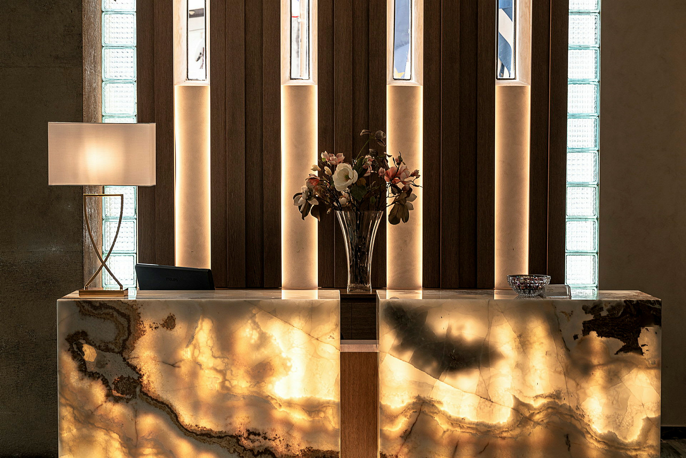 En receptionsdisk med en dekorativ belysning, en vas med blommor och en lampa. (AI-genererad text)
