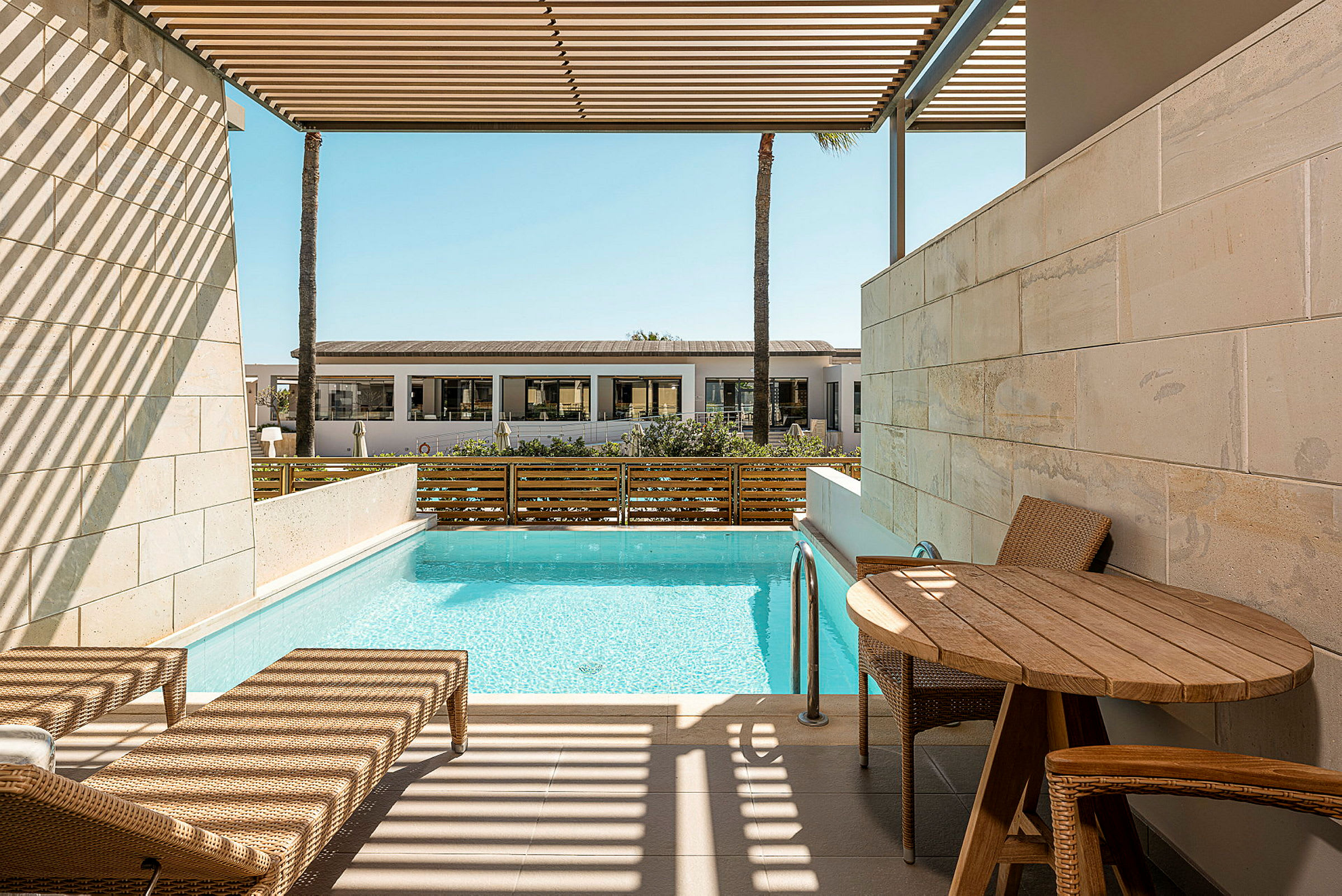 En privat terrass med solstolar, ett bord och pool, med utsikt över en byggnad på avstånd. (AI-genererad text)