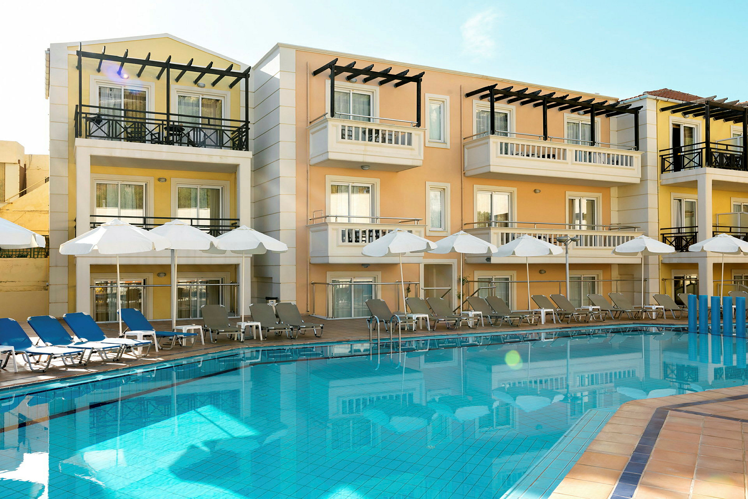 Hotellbyggnad med balkonger, solstolar vid en pool. (AI-genererad text)