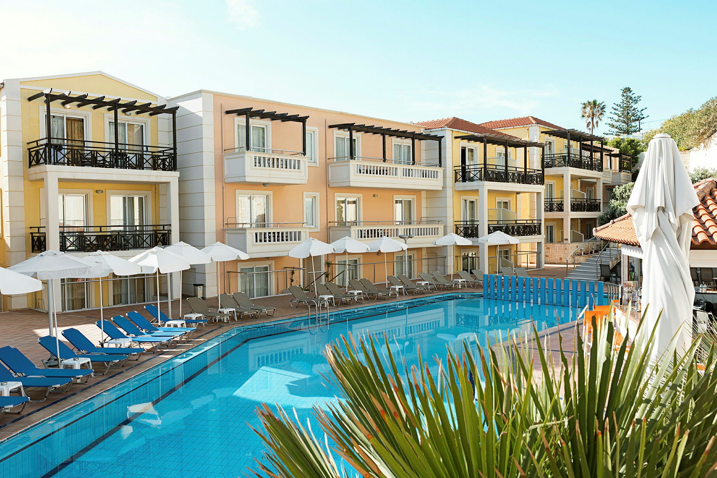 Hotellbyggnader med balkonger runt en swimmingpool och poolområde med solstolar och parasoll. (AI-genererad text)