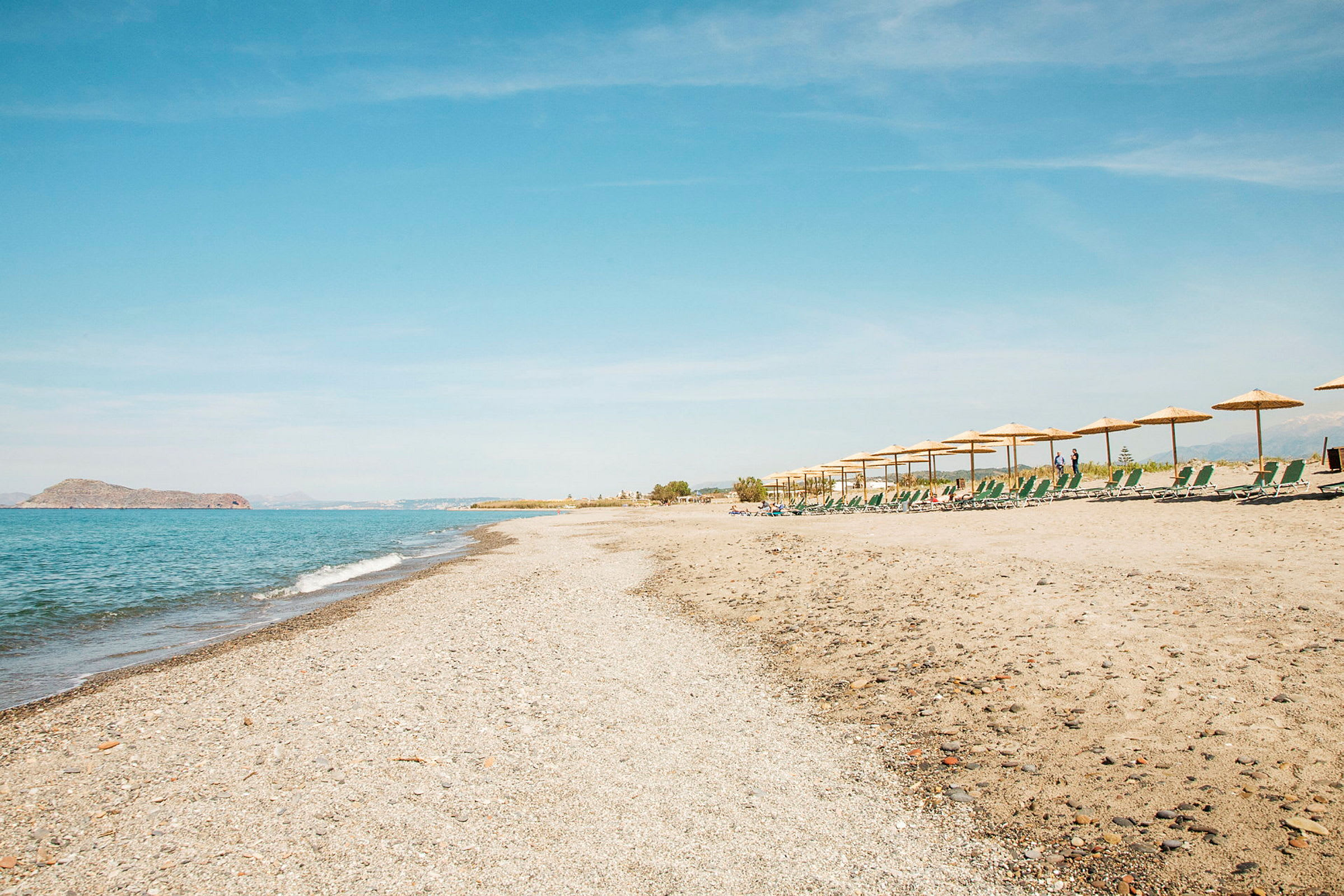 En sandstrand med solstolar och parasoller längs kanten. (AI-genererad text)