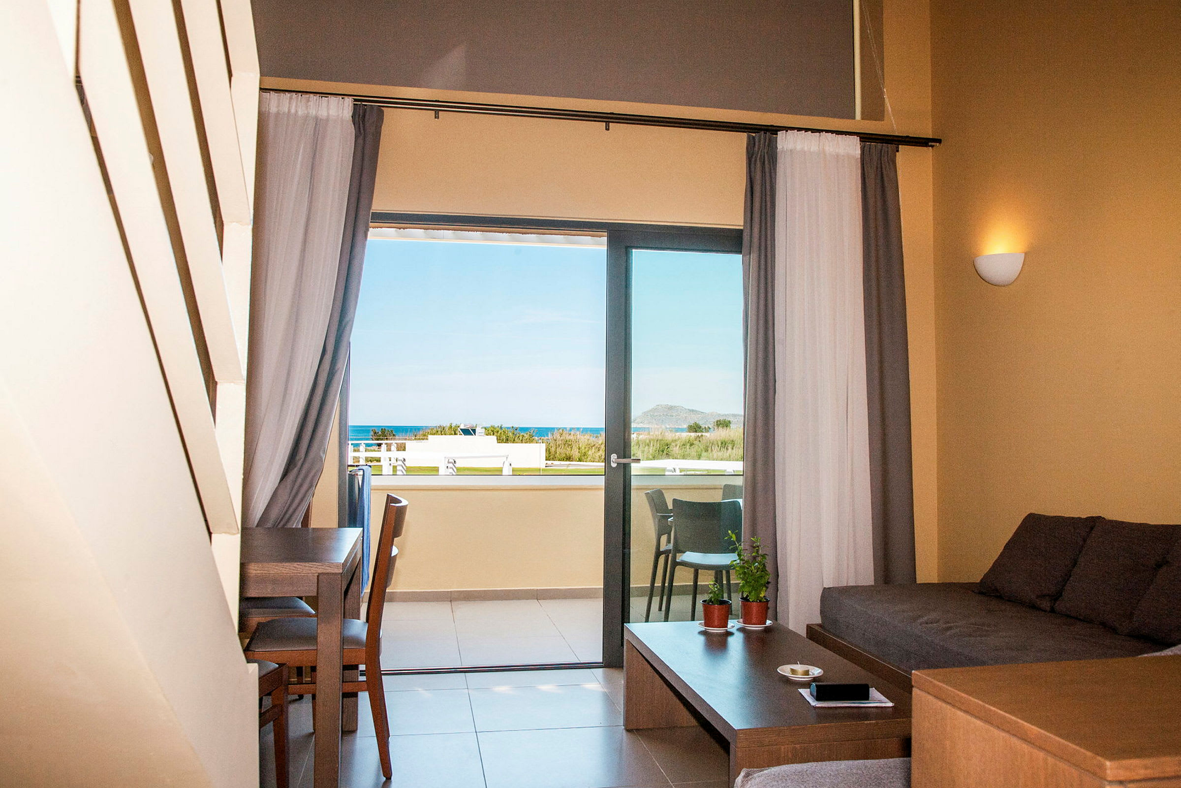 Utsikt från ett hotellrum med sittgrupp och balkong där man ser havet. (AI-genererad text)