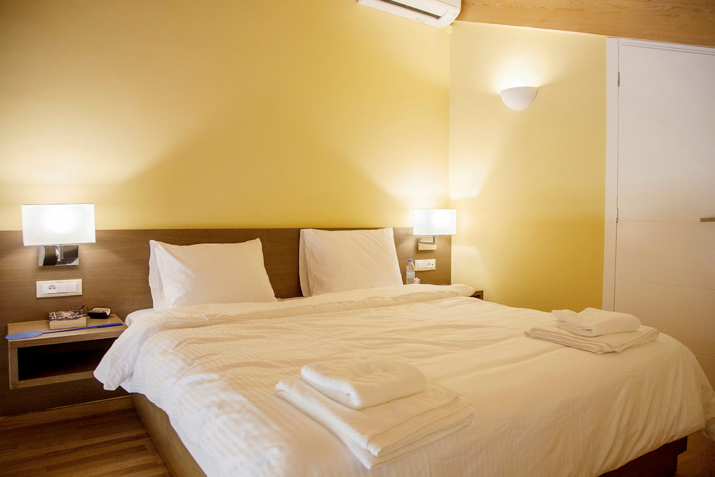 Ett hotellrum med en dubbelsäng, vita sängkläder och gula väggar. (AI-genererad text)