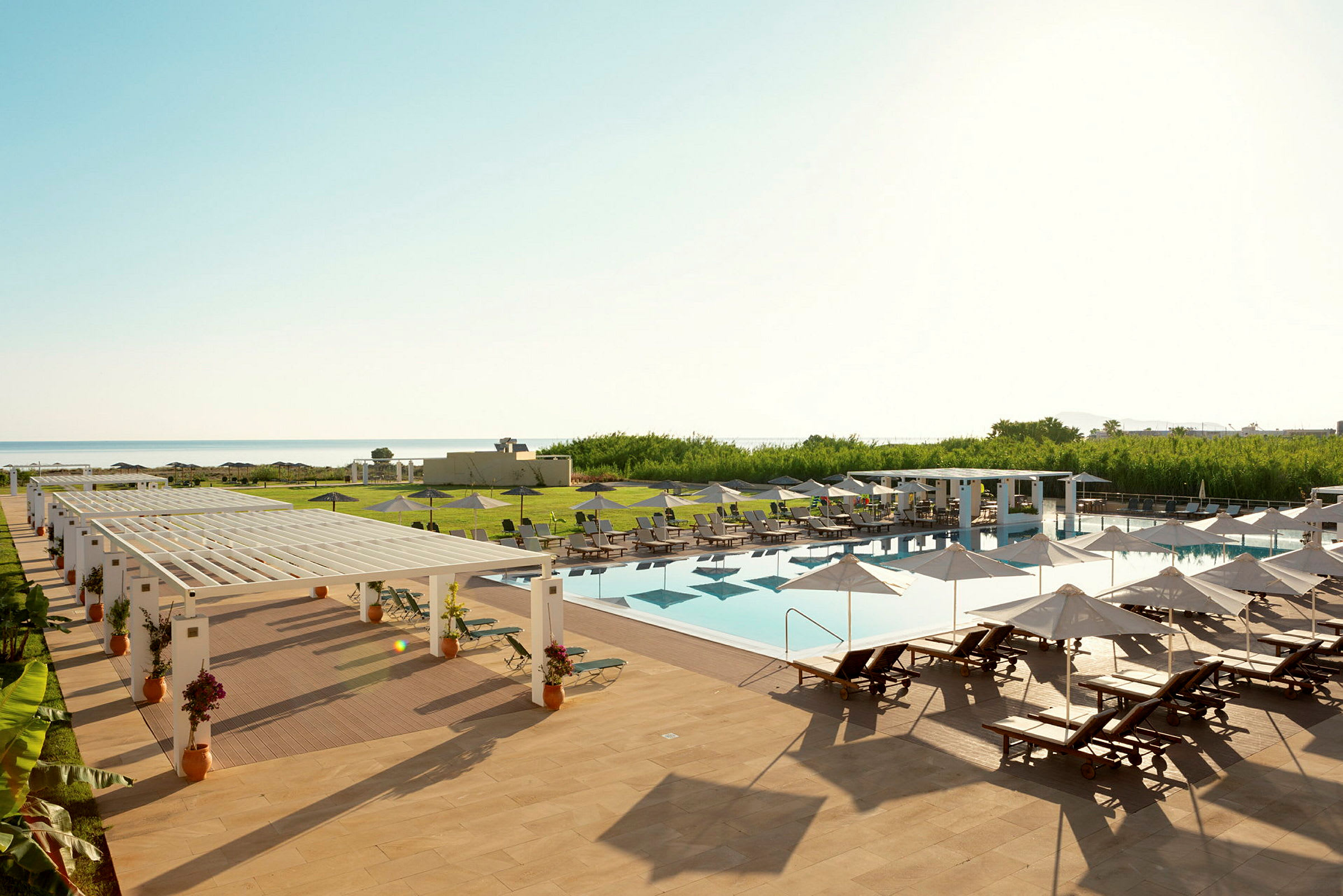 En utomhuspool med solstolar och parasoller på ett hotellområde vid havet. (AI-genererad text)