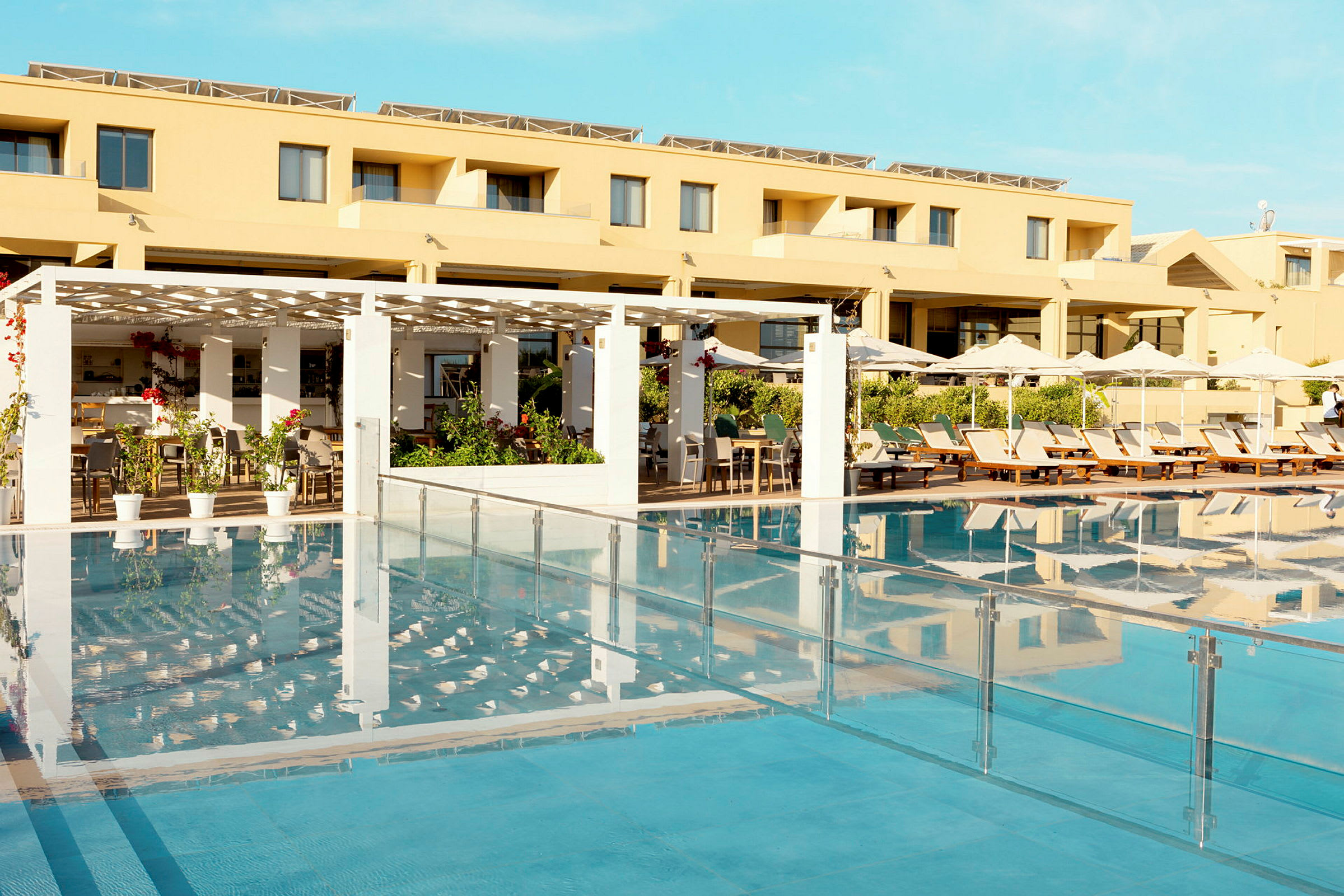 Hotellfasad med pool och solstolar i förgrunden. (AI-genererad text)