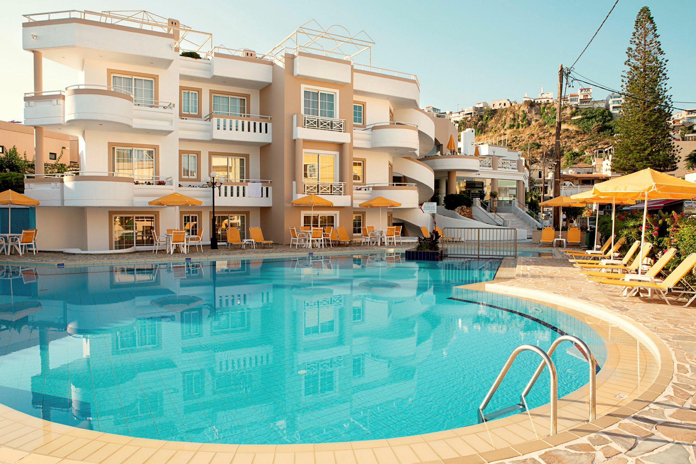 Bild av ett hotell med en pool och solstolar framför byggnaden. (AI-genererad text)