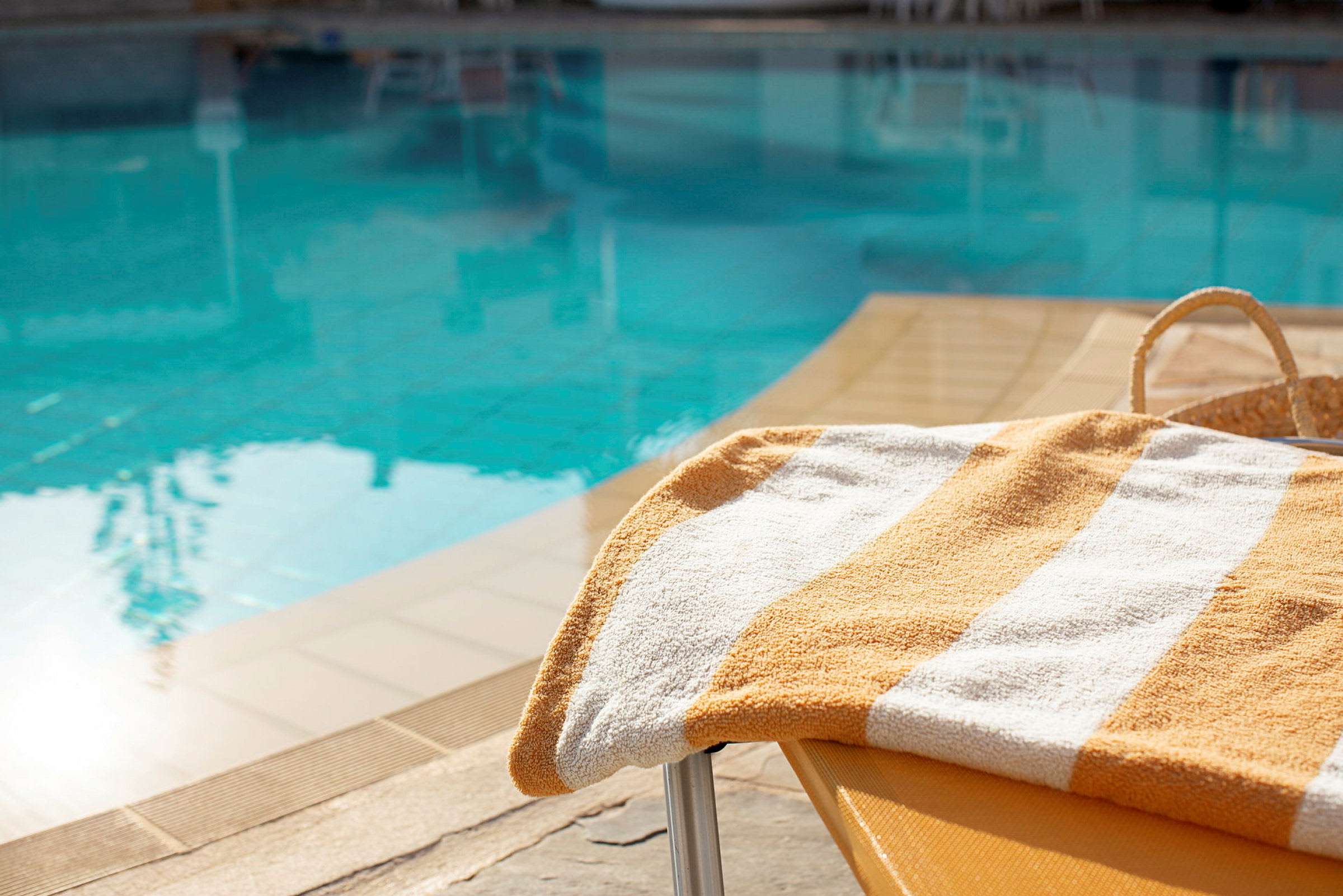 En gulrandig handduk ligger på en solstol vid en pool. (AI-genererad text)