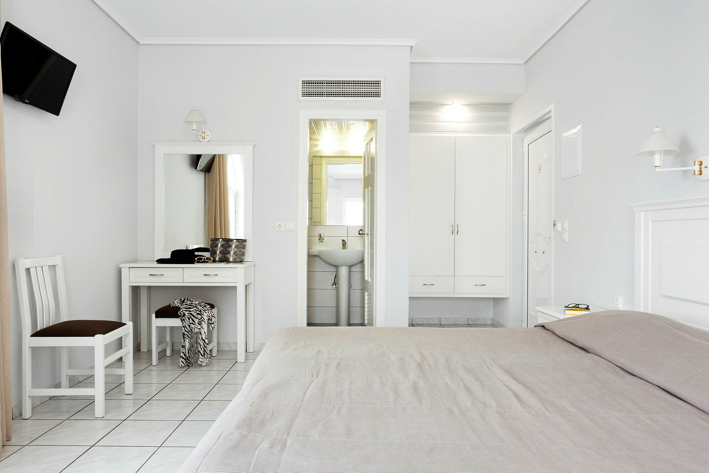 Ett ljust hotellrum med ett skrivbord, stol och säng, samt en garderob och ett badrum. (AI-genererad text)