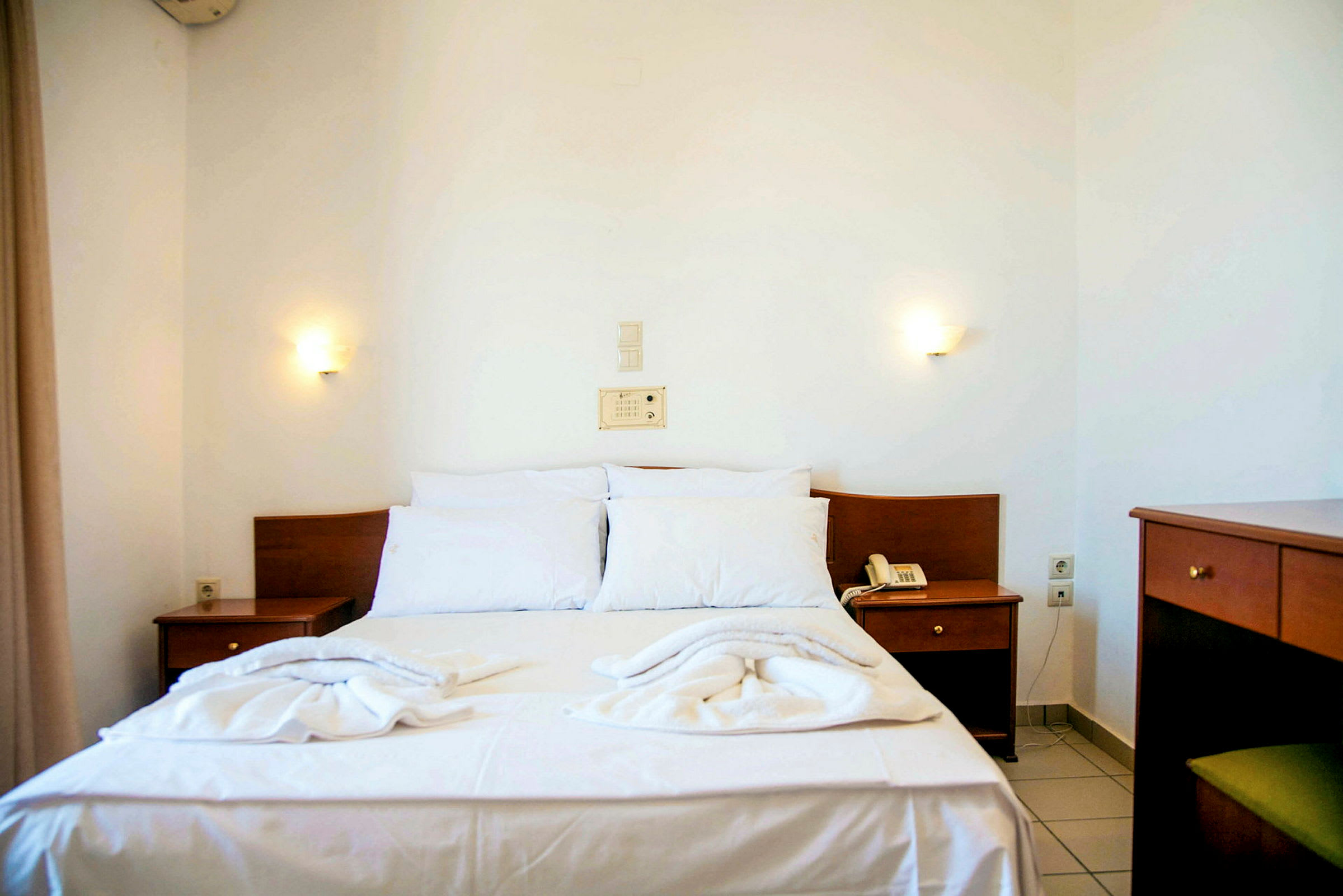Ett hotellrum med en dubbelsäng med vita lakan och trädetaljer. (AI-genererad text)
