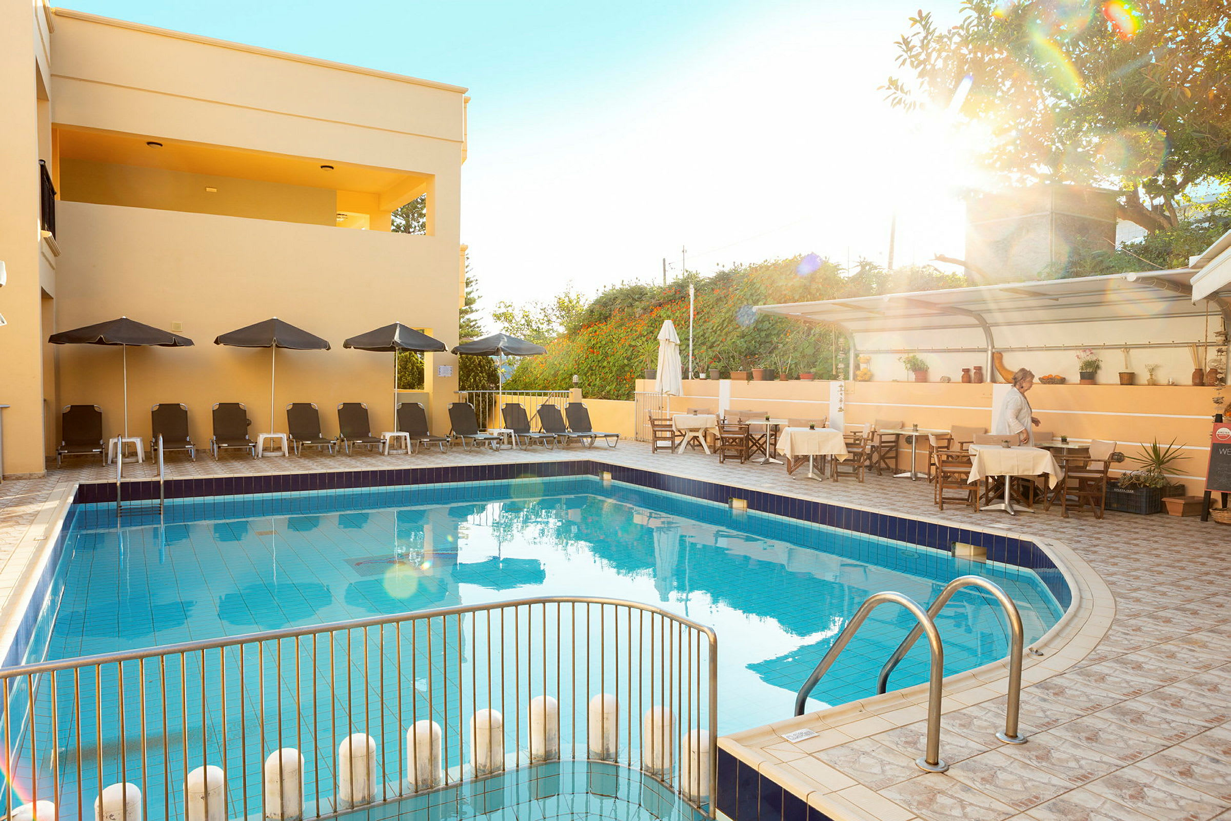 En pool vid ett hotell med solstolar, parasoller och ett matområde vid sidan av. (AI-genererad text)