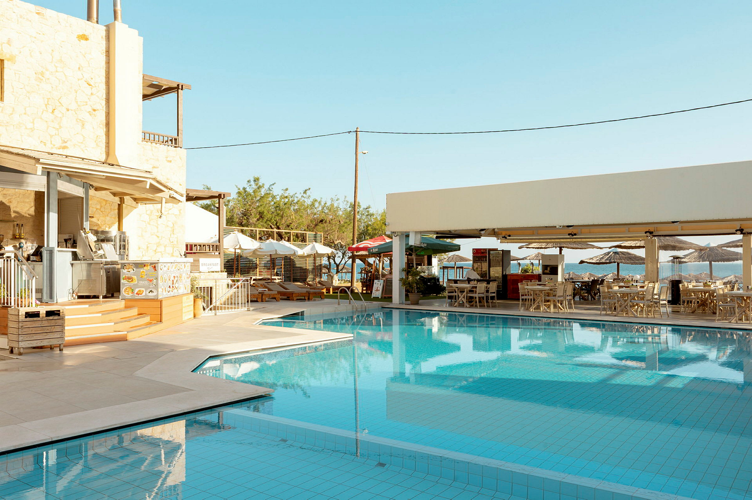Bild av en utomhuspool bredvid restauranger och sittplatser, omgiven av solstolar och parasoller. (AI-genererad text)