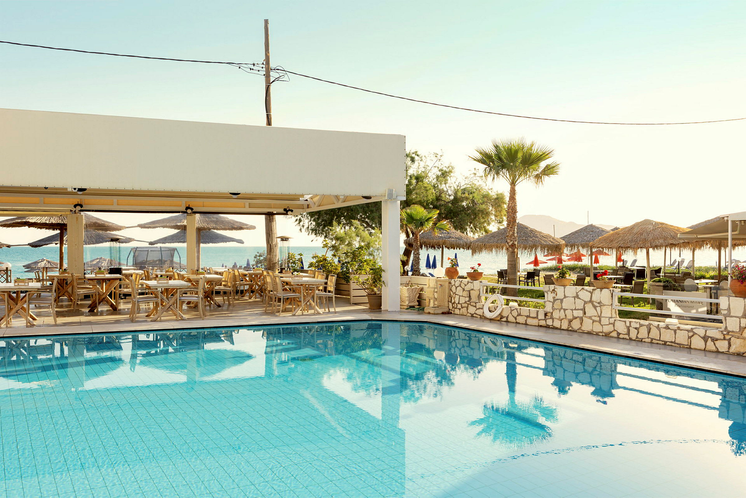 En utomhuspool med sittmöbler under en skuggande pergola och utsikt mot havet. (AI-genererad text)