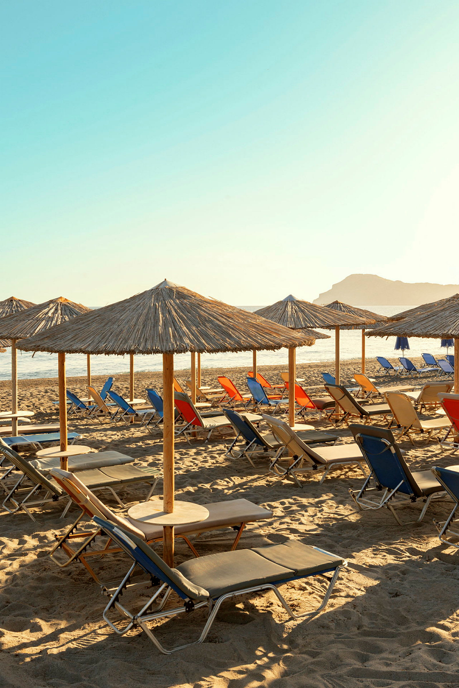 Strand med solstolar och halmparasoller under klar himmel. (AI-genererad text)