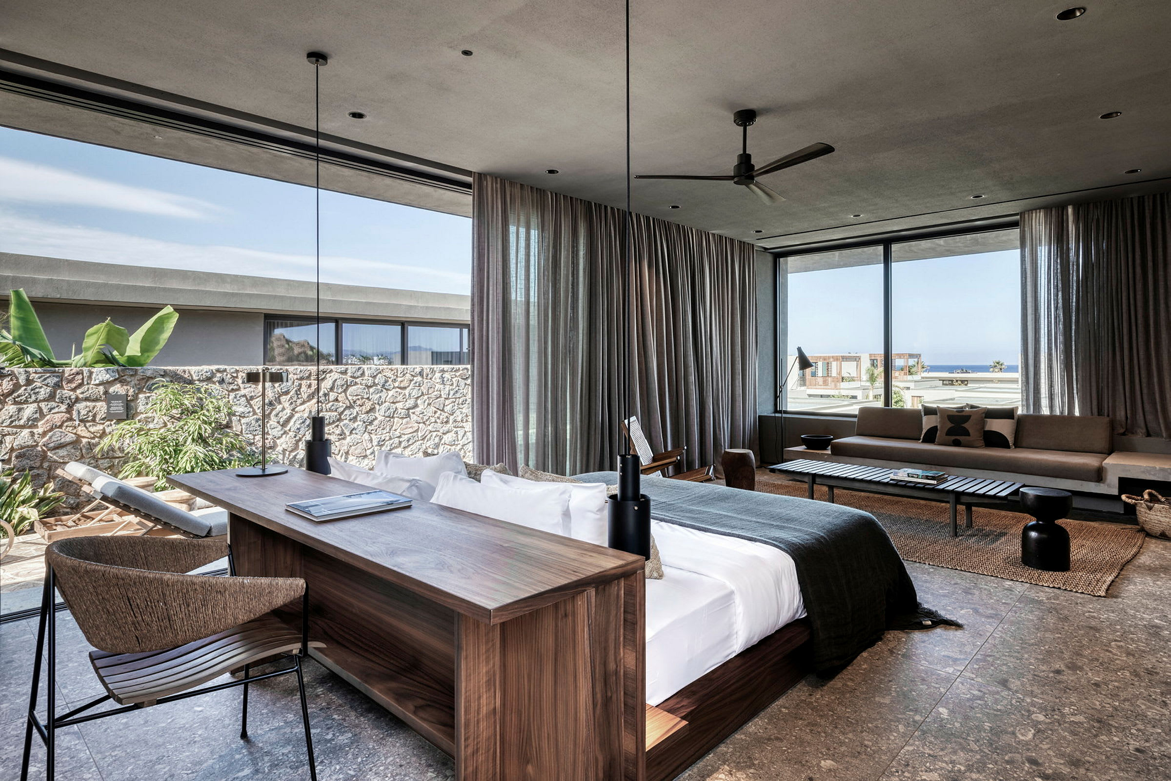 Modern hotellsvit med stor säng, skrivbord och sittutrymme. Fönster med utsikt mot havet och grönska. (AI-genererad text)