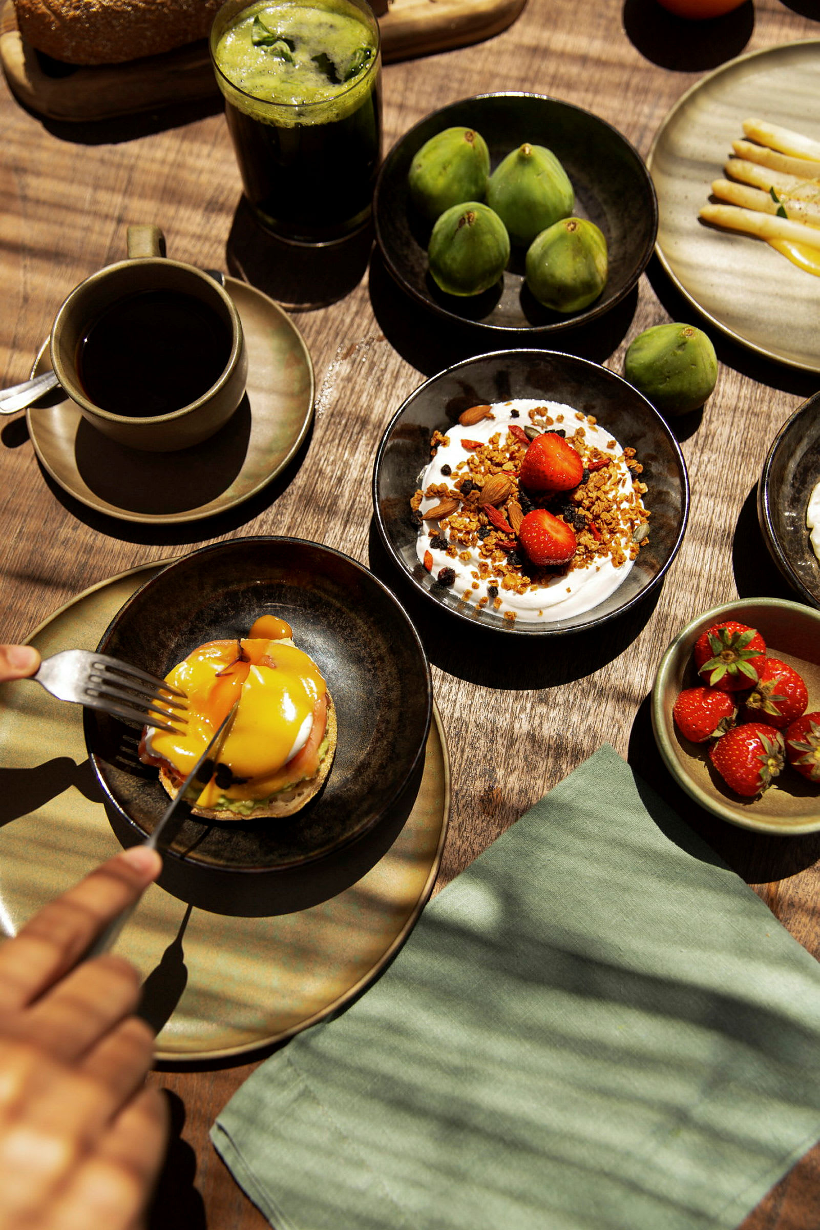 Frukost med kaffe, gröna fikon, müsliyoghurt, jordgubbar och en engelsk muffins med ägg och sås. (AI-genererad text)